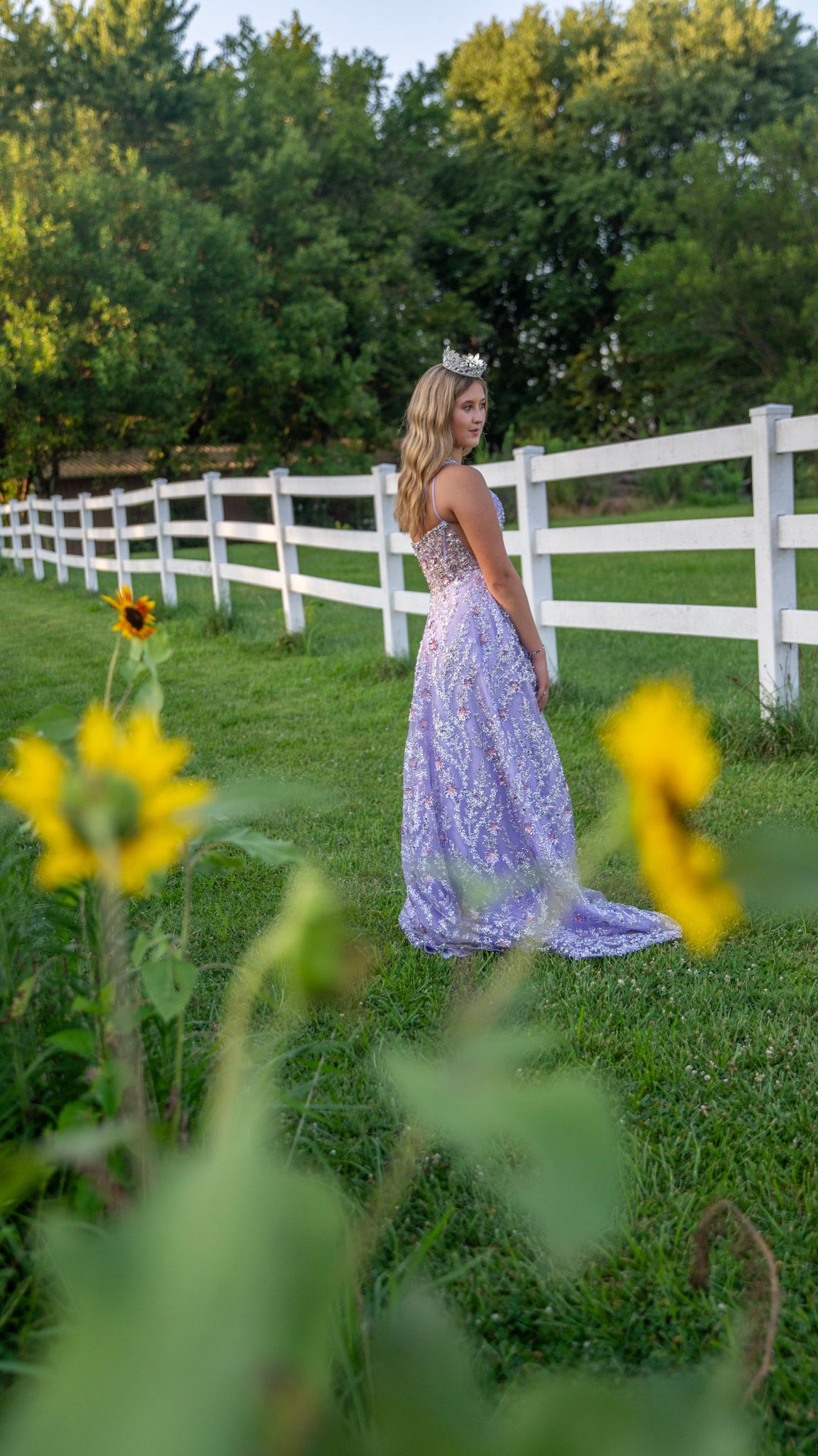 Sunflowers frame a purple formal dress against a white fence in a country setting.