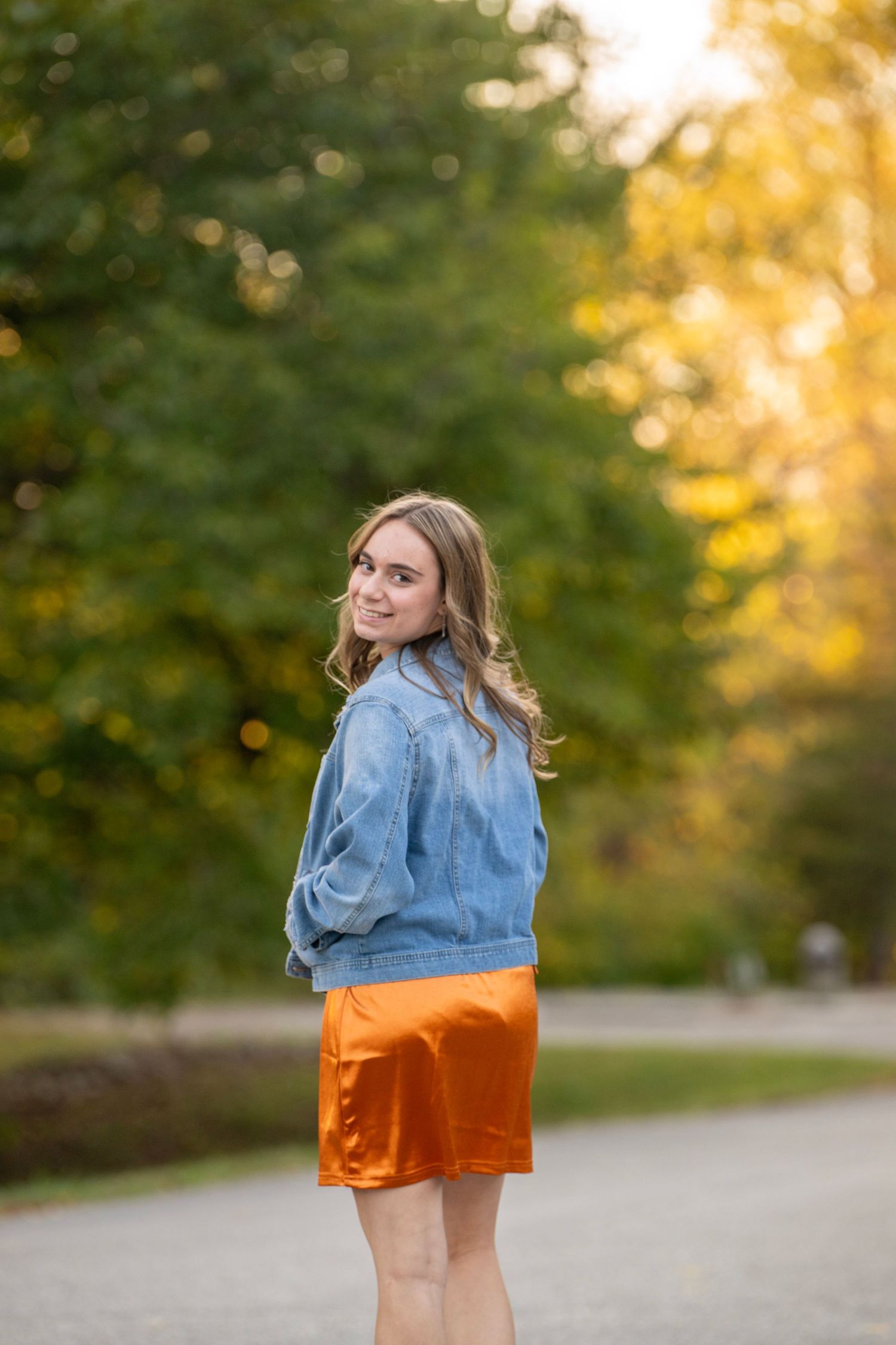Someone in denim and orange clothing poses playfully during a golden hour photoshoot.