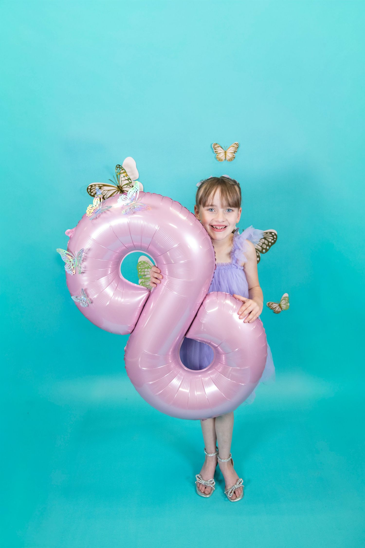 Pink metallic number 2 balloon with decorative butterflies against turquoise wall.
