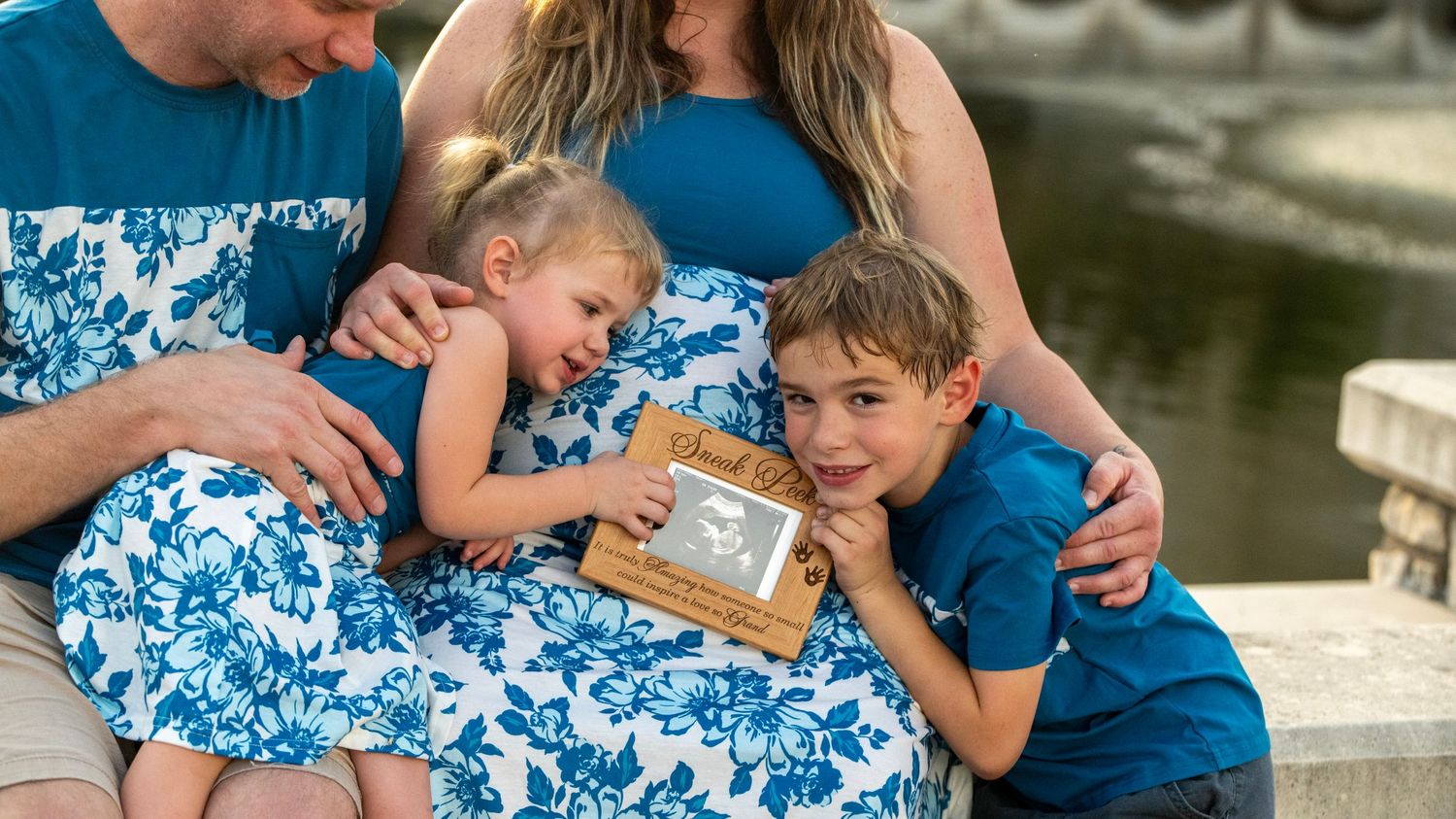 Family members in blue attire sharing close moments by a stone bridge and water feature.