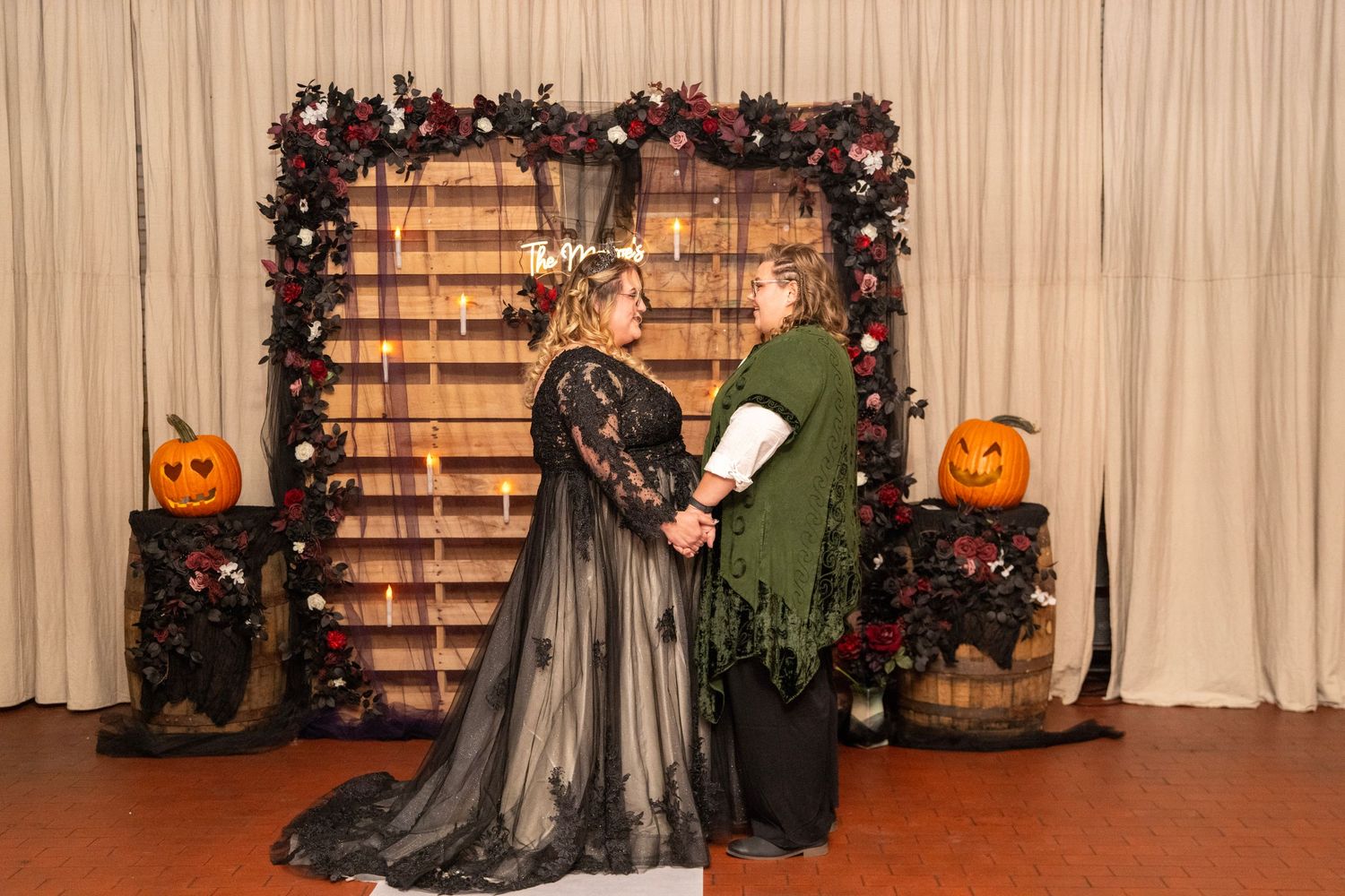 Halloween themed event setup with floral arches, pumpkins and draped curtains.