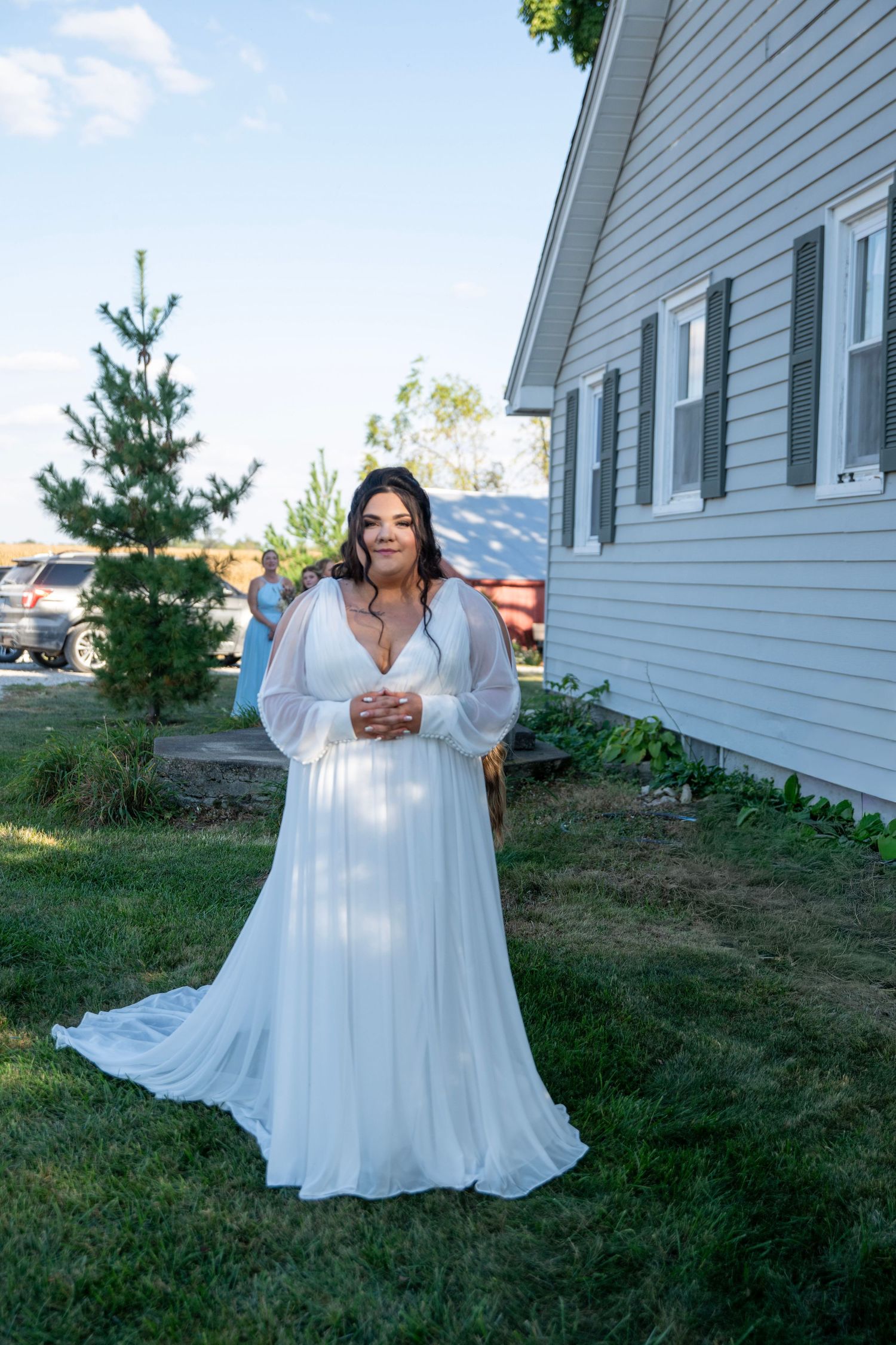 Person in flowing white dress poses gracefully on grassy lawn near white house exterior.