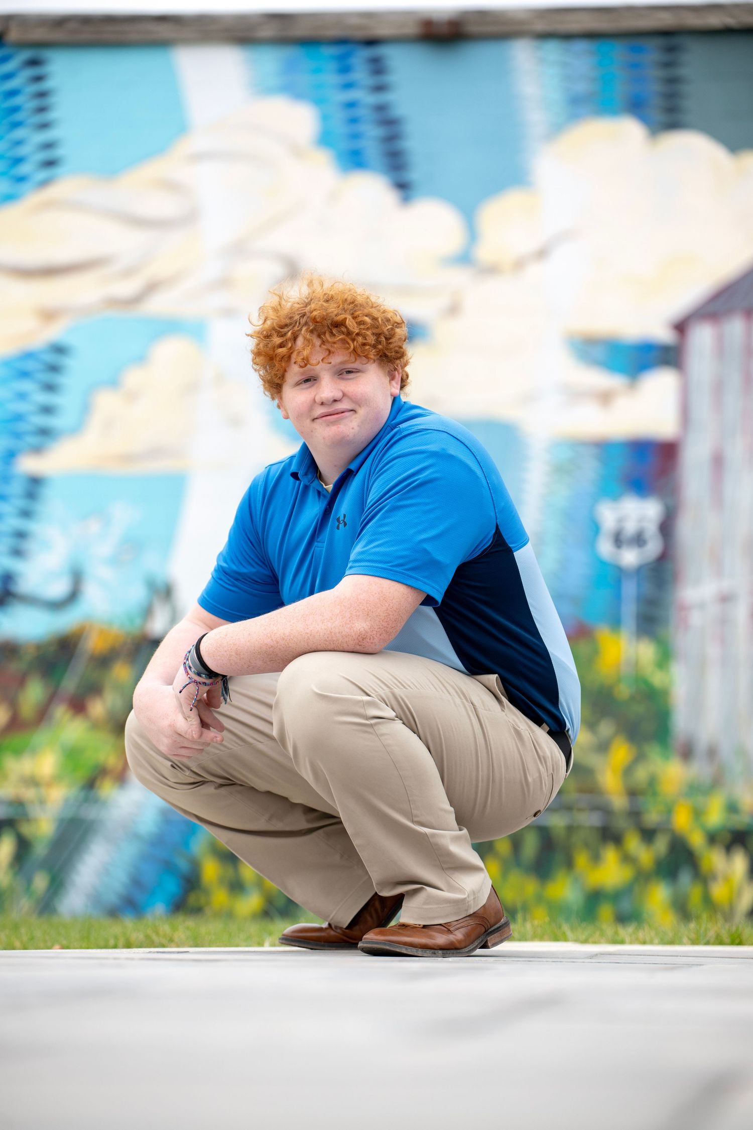 Casual crouching poses against colorful mural background in blue polo and khakis.