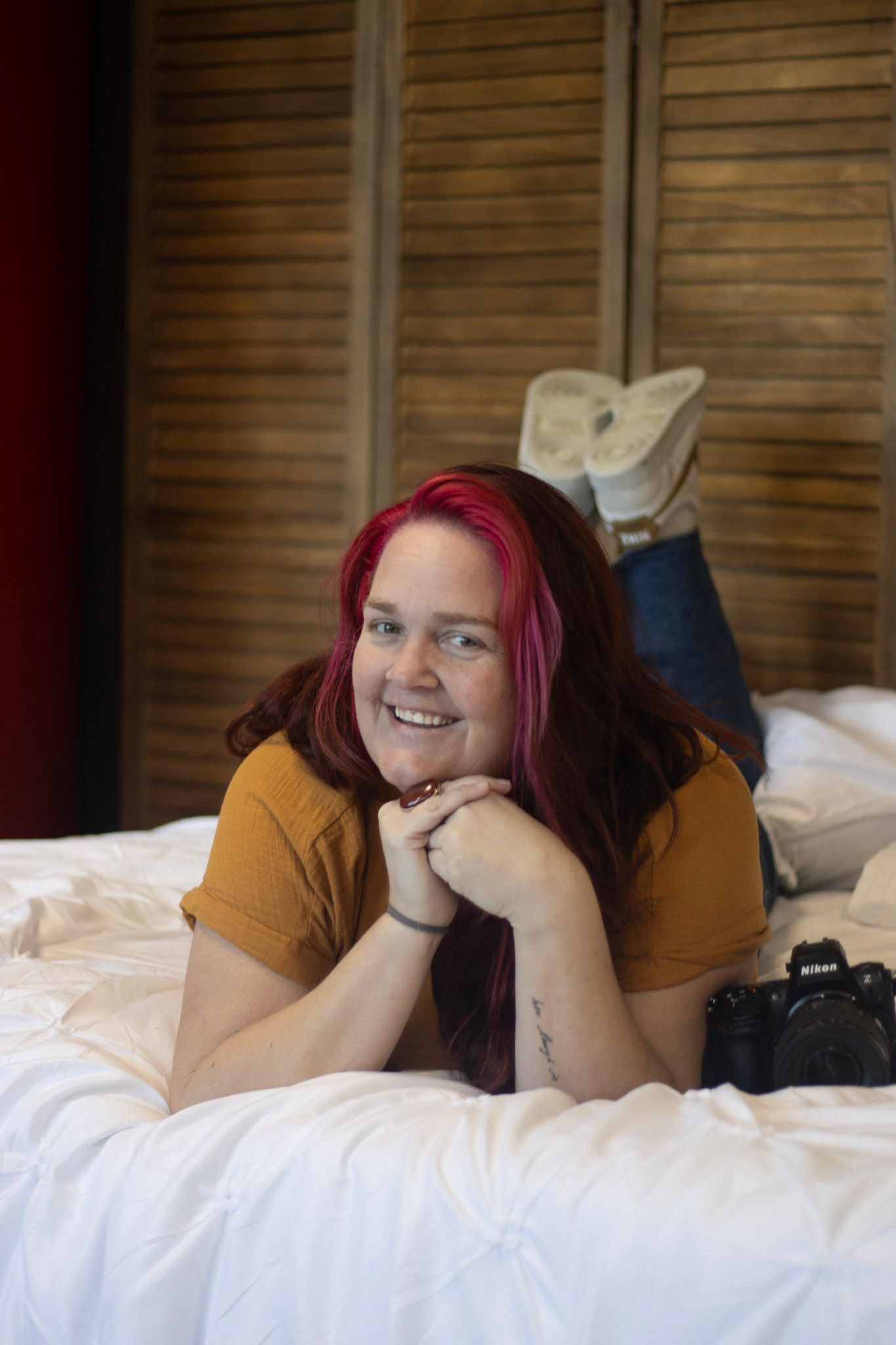 Casual portrait on white bedding with camera and bright red hair.
