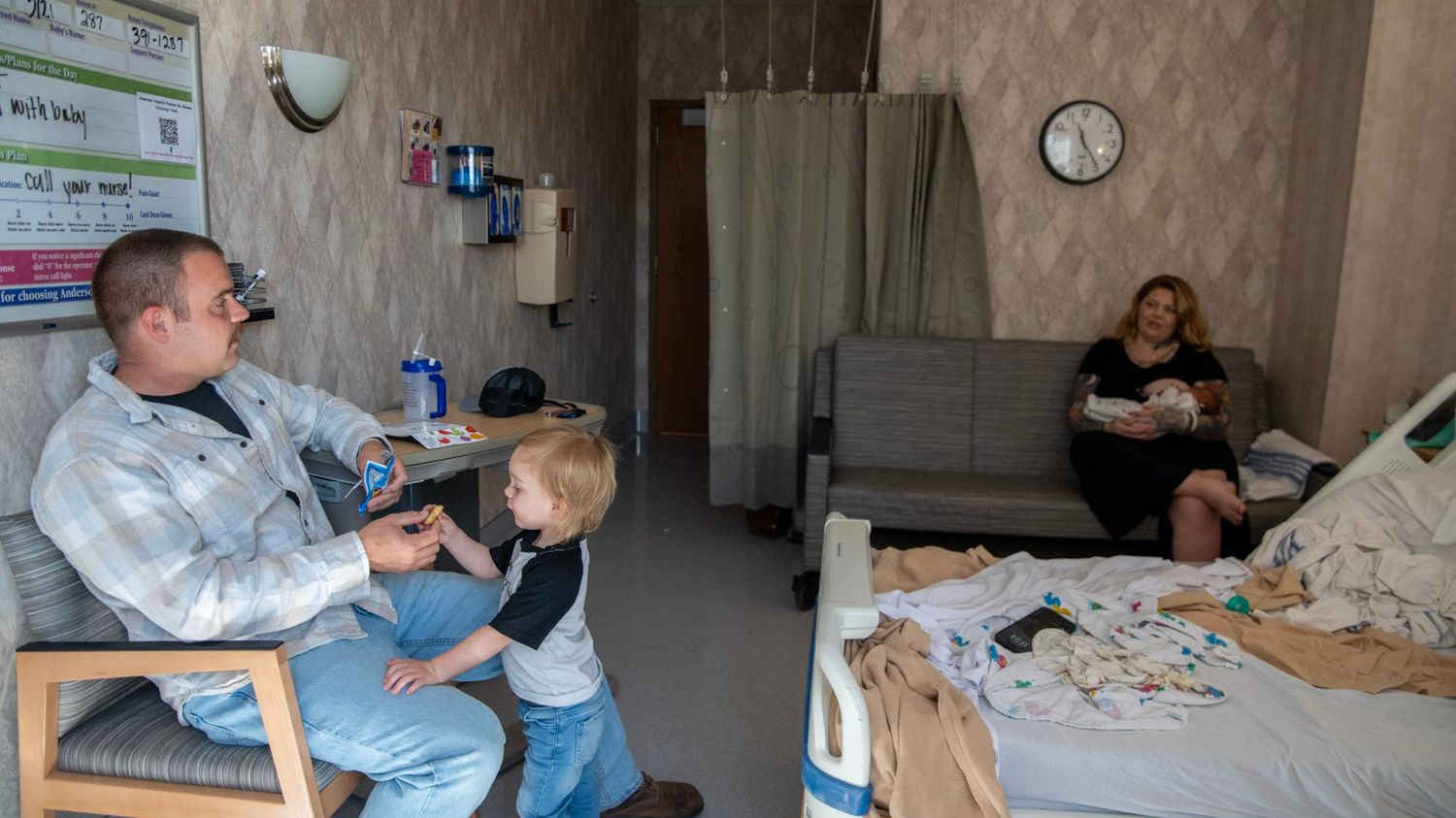 Hospital room setting with medical equipment and people interacting with a newborn.
