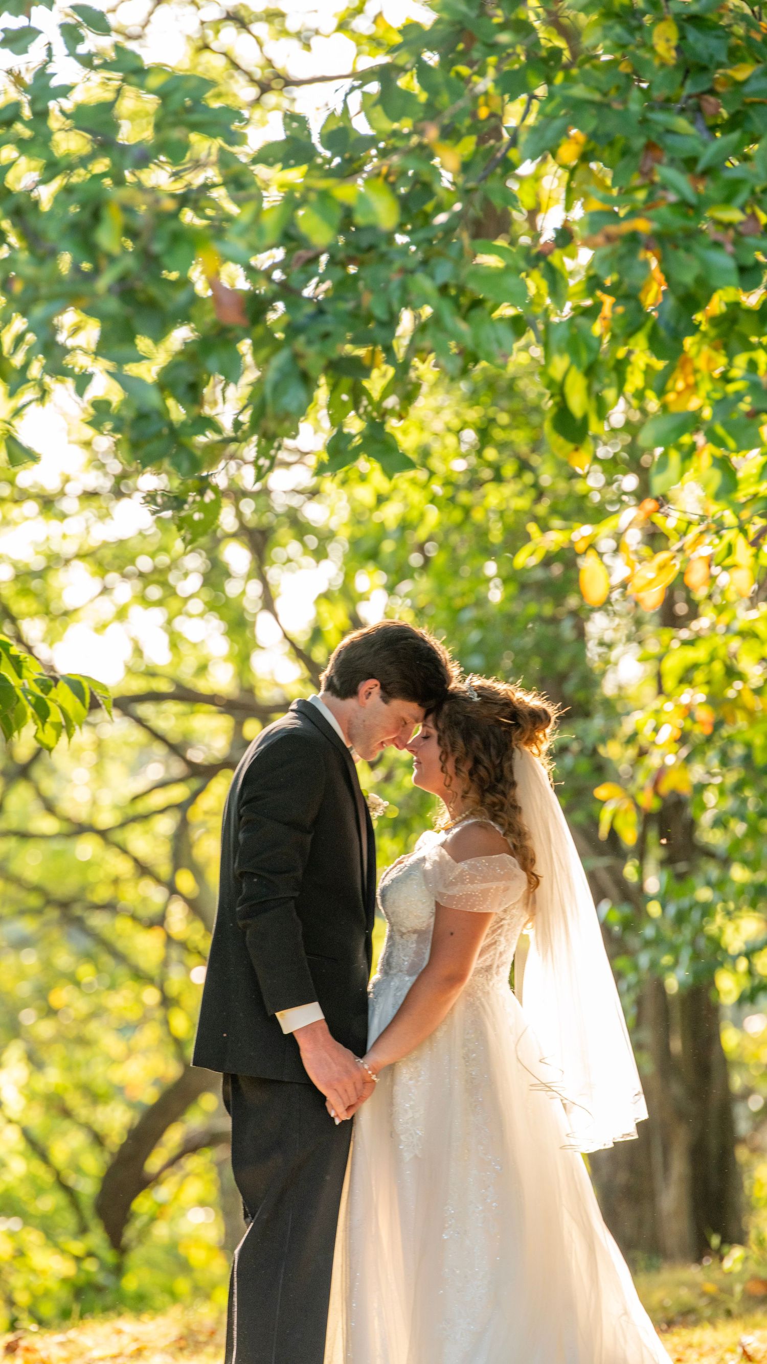 Newlyweds share intimate moments in a sunlit garden setting wearing traditional wedding attire.