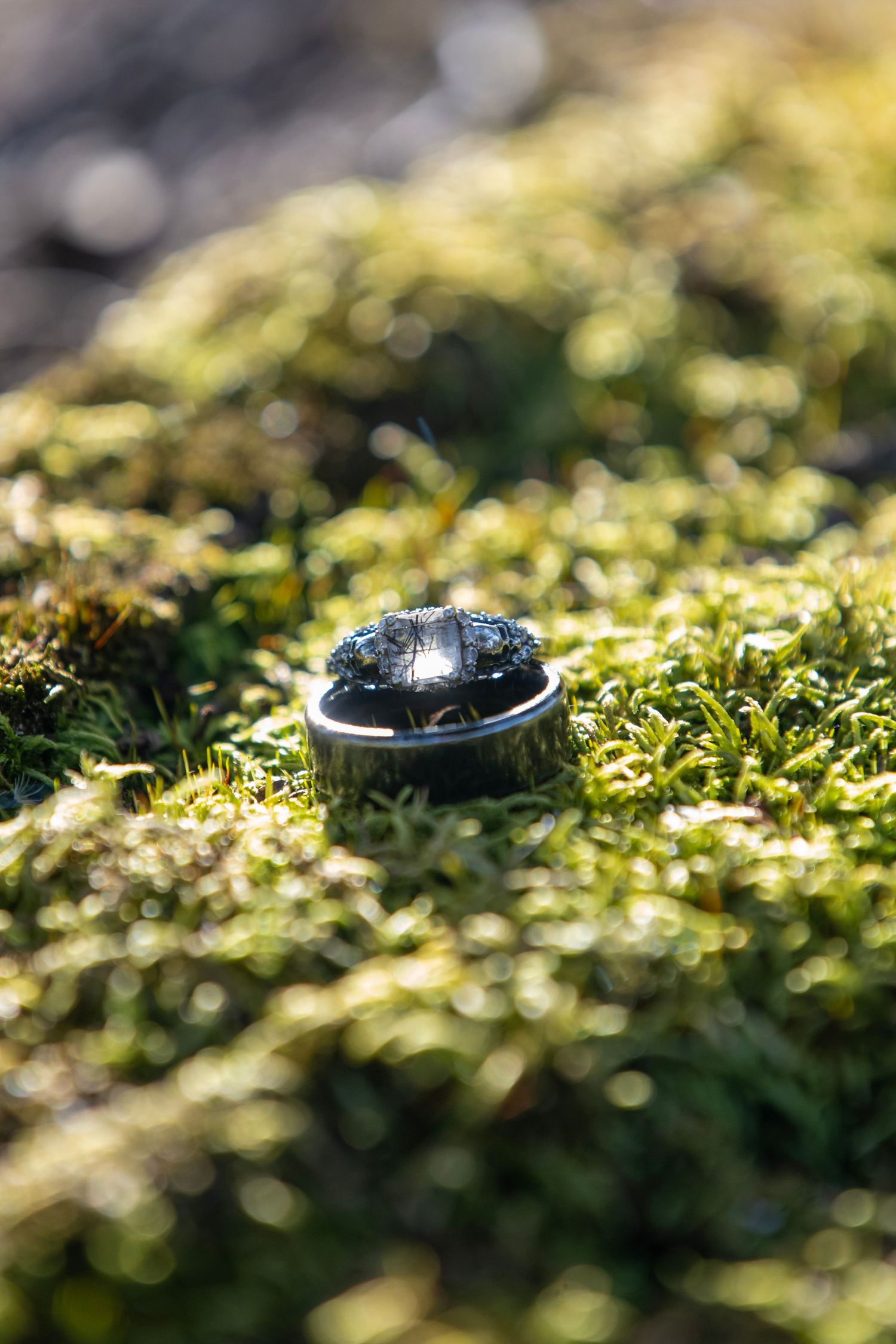 Close-up of a wedding ring nestled in green moss with shallow depth of field.