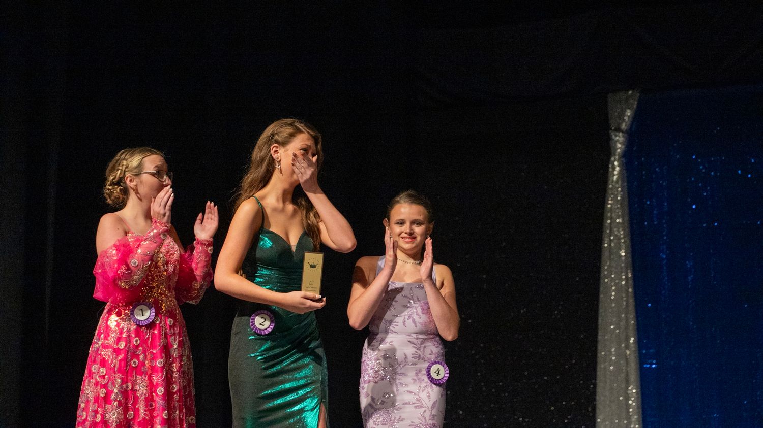 Contestants react emotionally during an awards ceremony on stage.