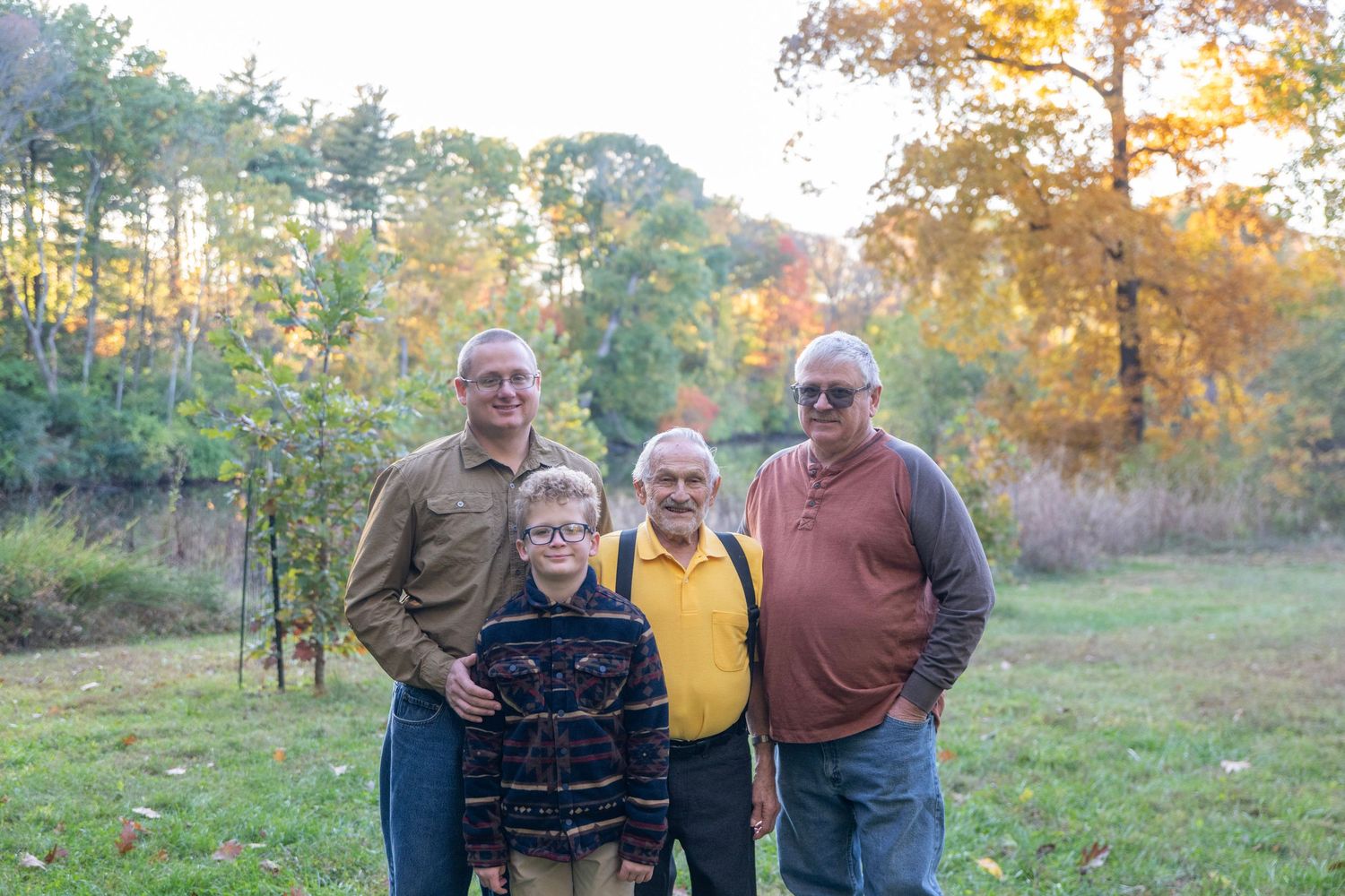 Small group poses together in casual attire against autumn landscape.