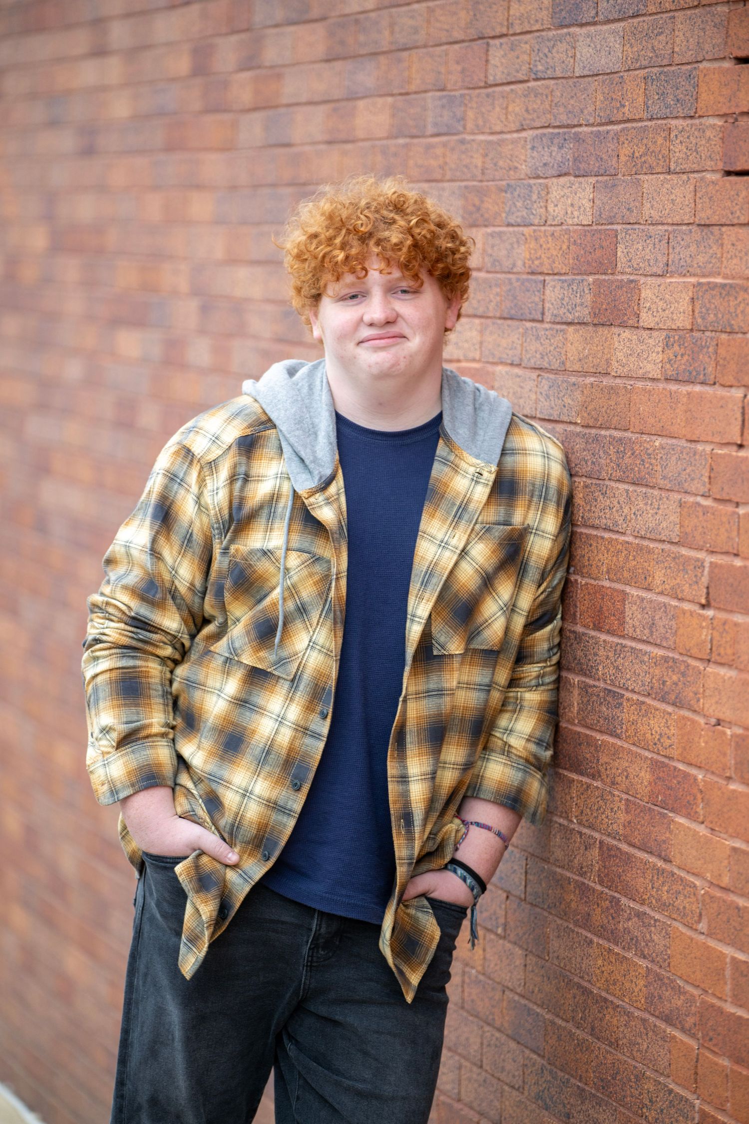Casual portrait session against red brick wall in plaid shirt and jeans.
