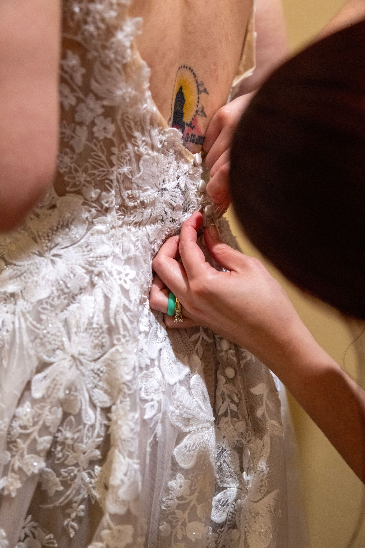 Hands carefully adjust the intricate lace details on a wedding dress.