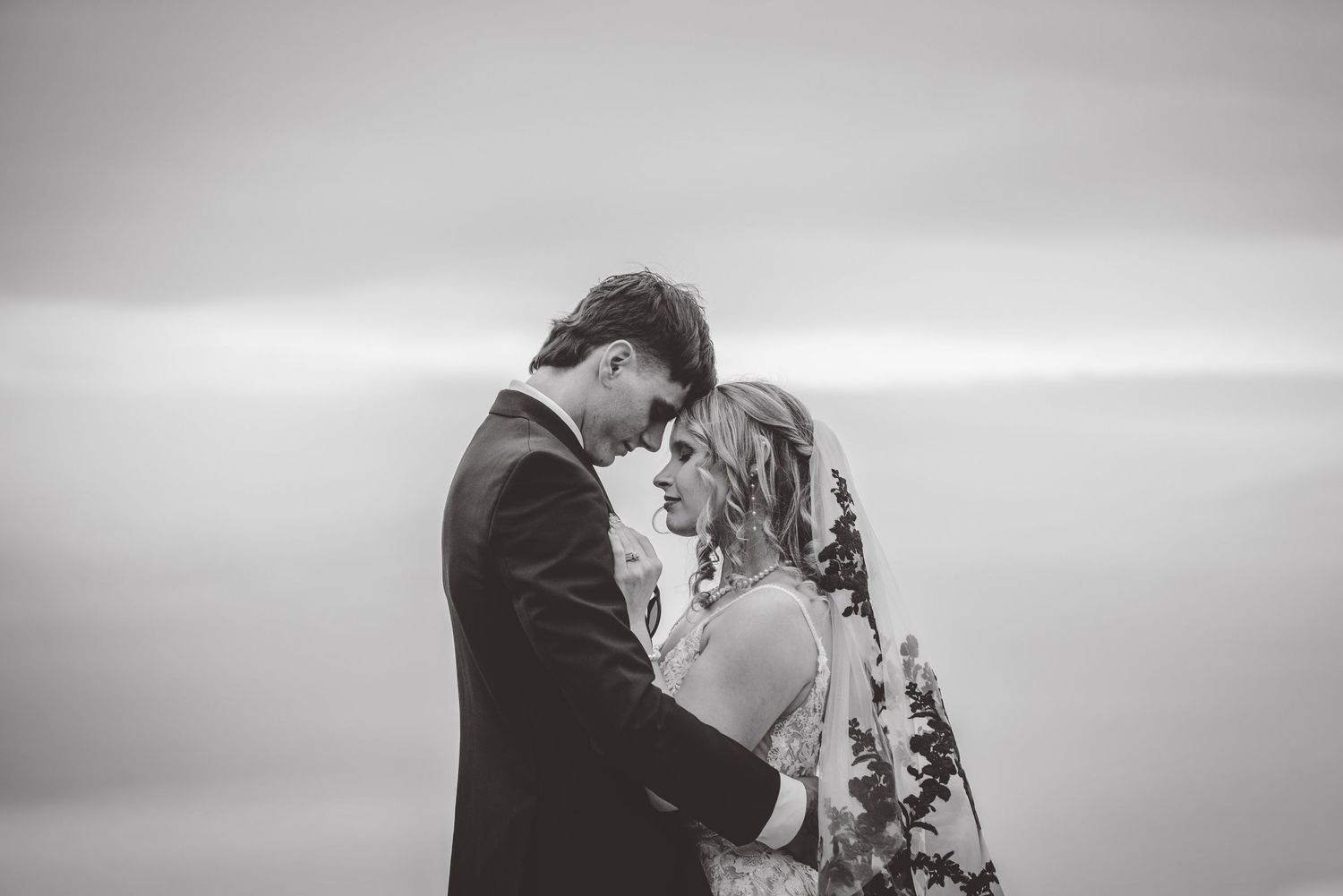 Dramatic black and white wedding portrait with soft lighting and intimate pose.