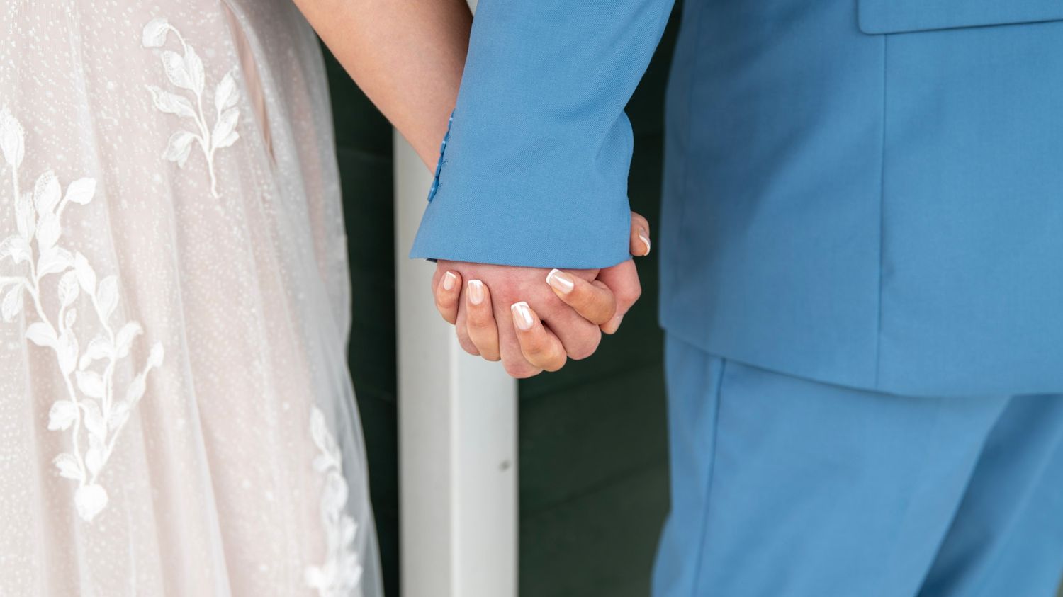 A couple shares their first kiss during an outdoor wedding ceremony under a rustic wooden arch.