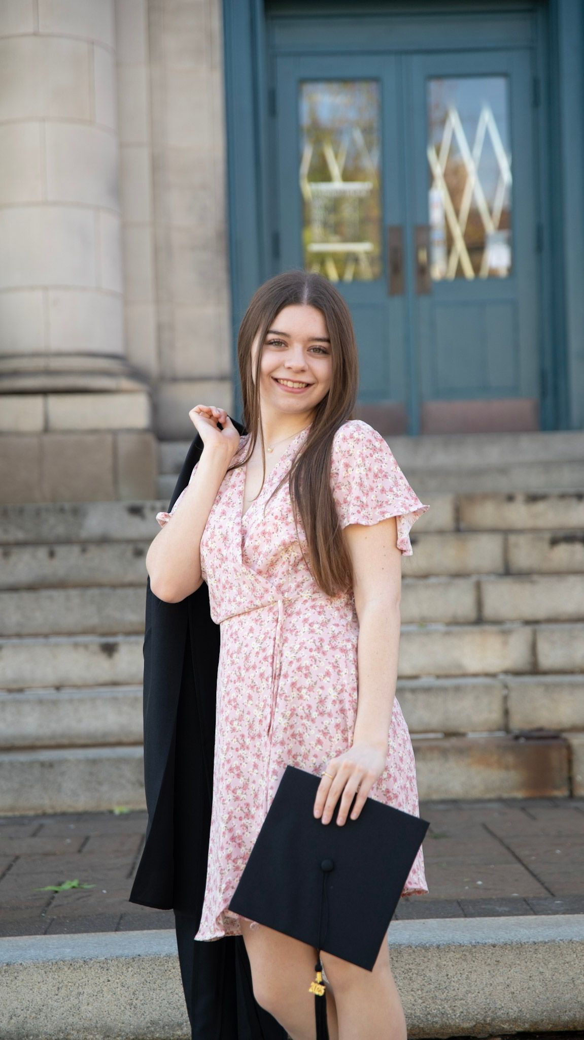 Graduate holding diploma poses in front of historic building with blue doors.