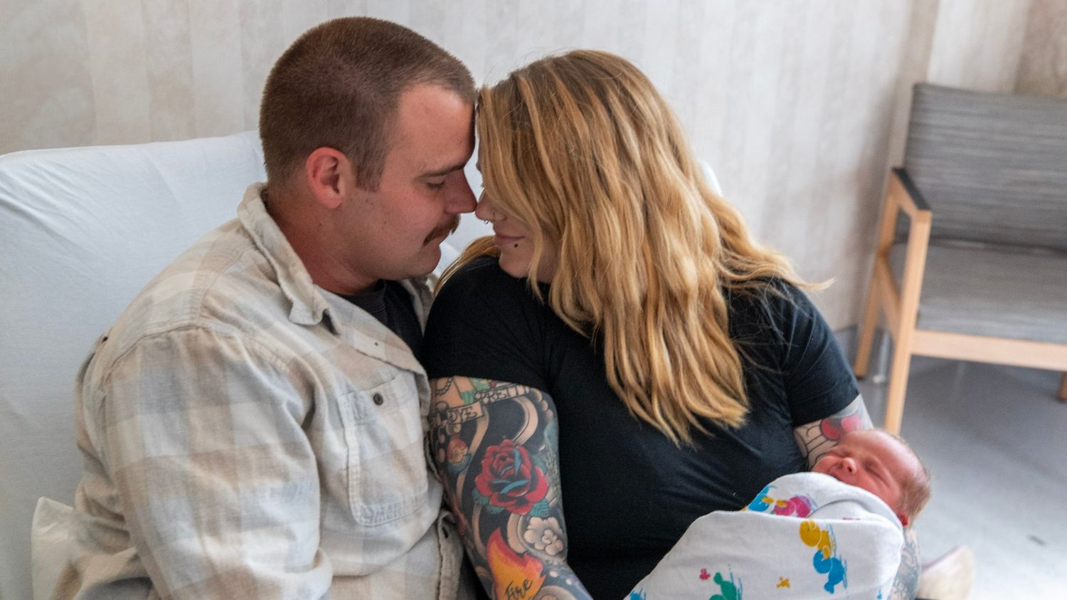 Parents sharing an intimate moment with their swaddled newborn in a medical setting.