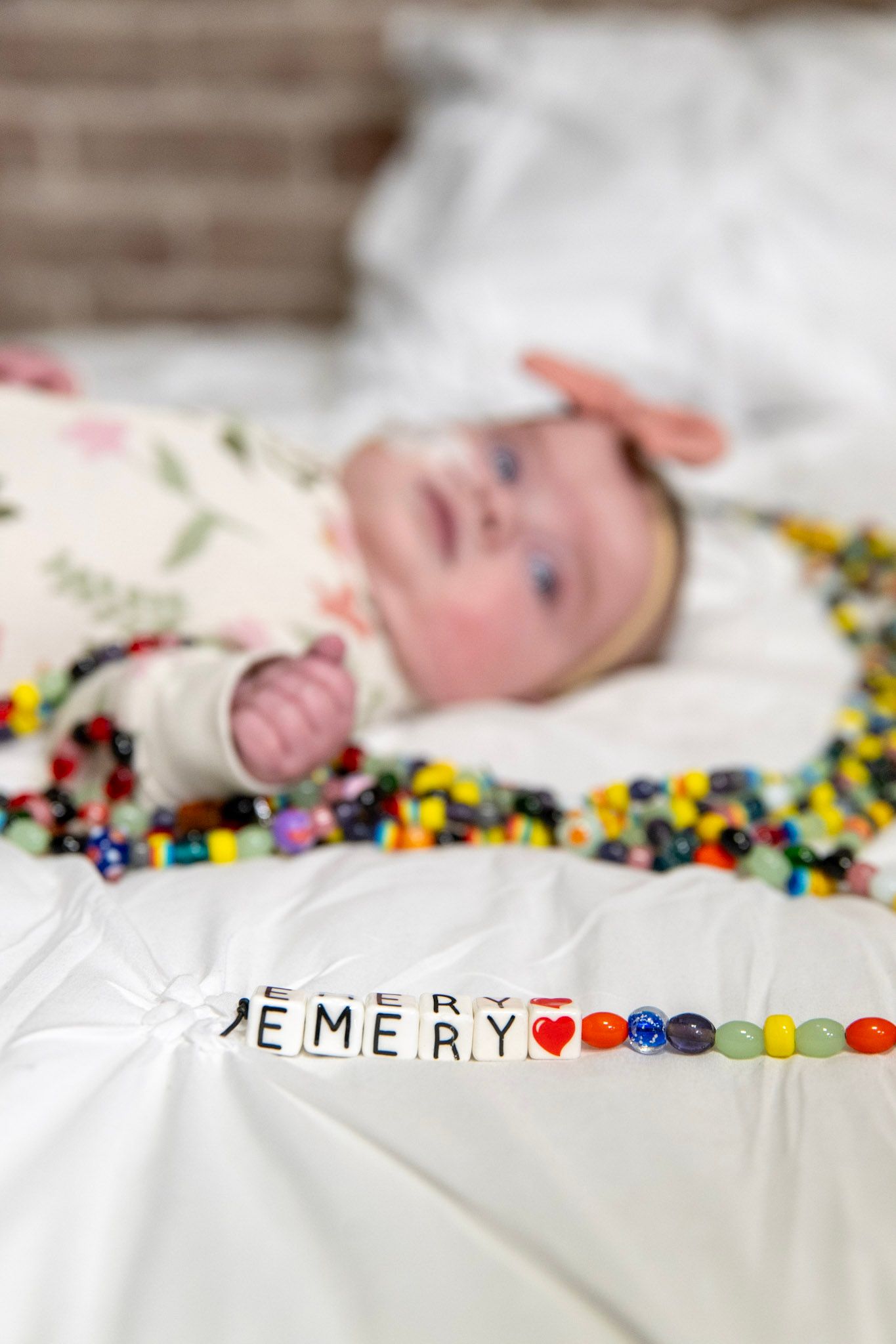 Baby portrait with decorative beaded name spelling 'Emery' on white background.