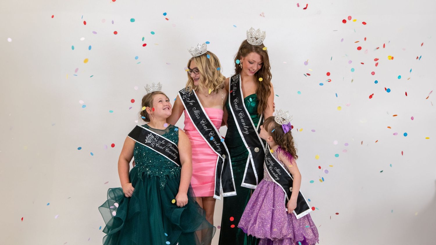 Three pageant contestants pose together as confetti falls during celebration photo.