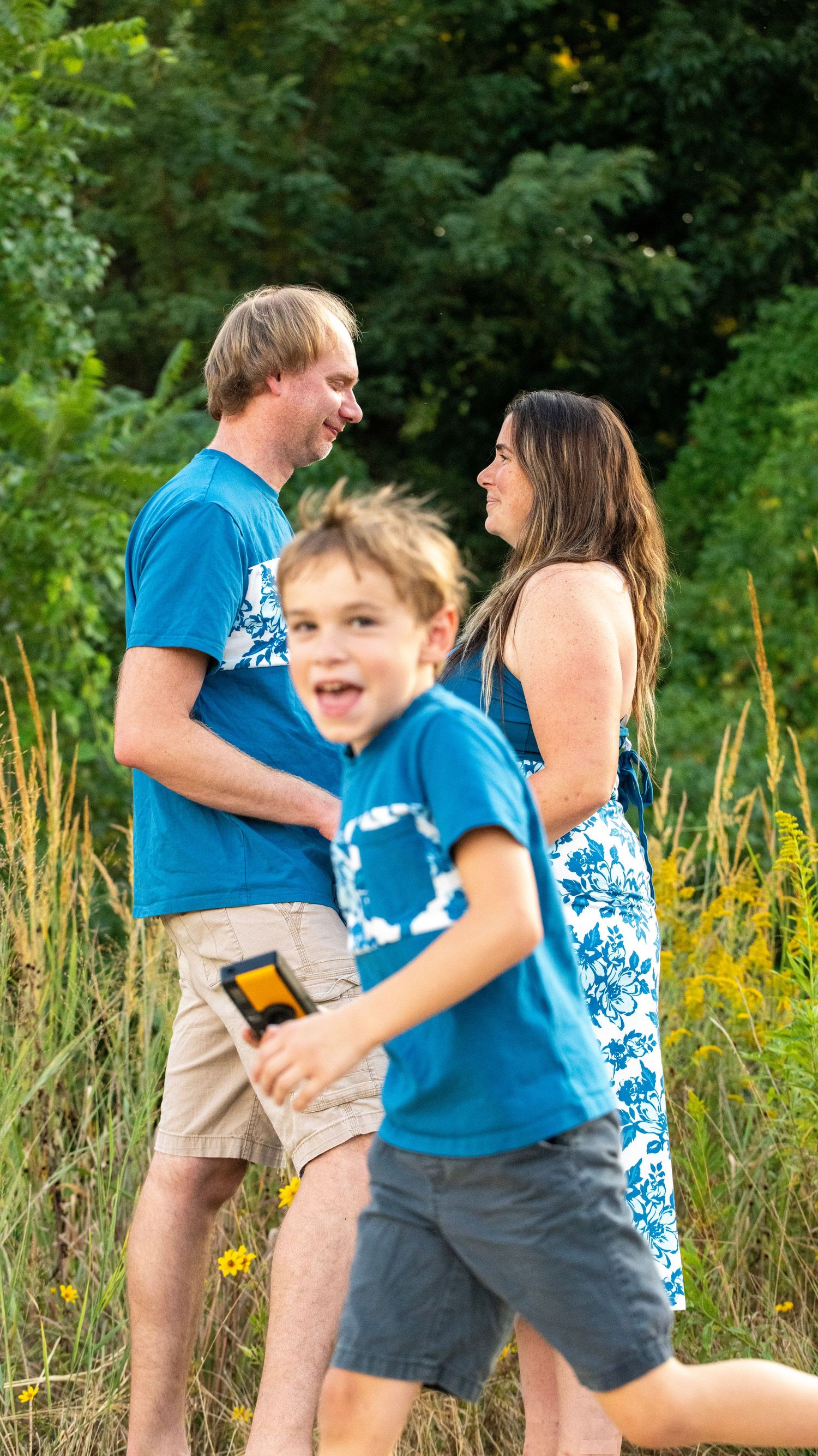 Family enjoying playful moments together in a grassy field wearing coordinating blue outfits.