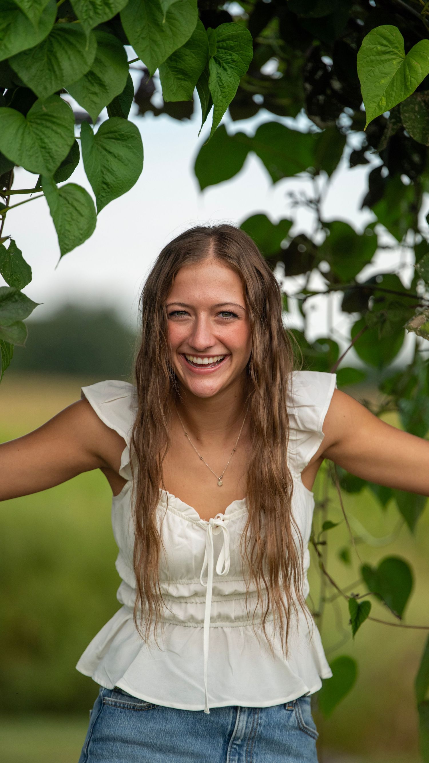 A joyful summer portrait under green leaves wearing a white peasant top.