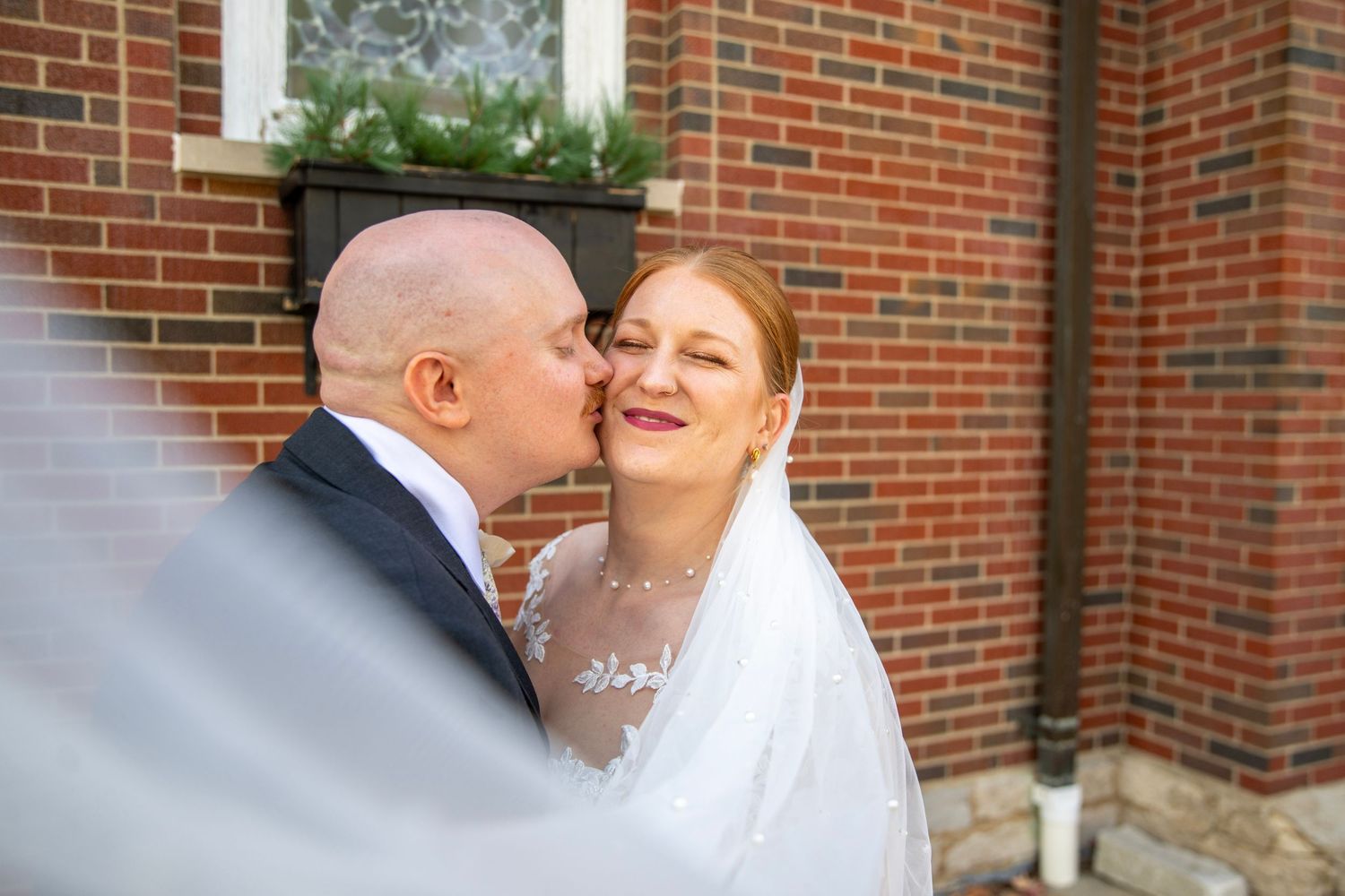 Wedding couple poses in front of a red brick church wall during their outdoor photo session.
