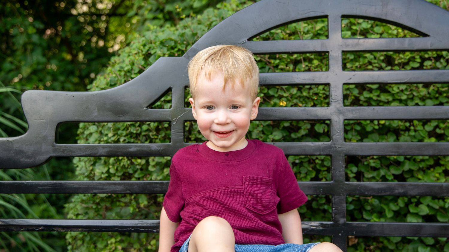 Multiple portraits on a park bench with decorative metal back against green foliage.