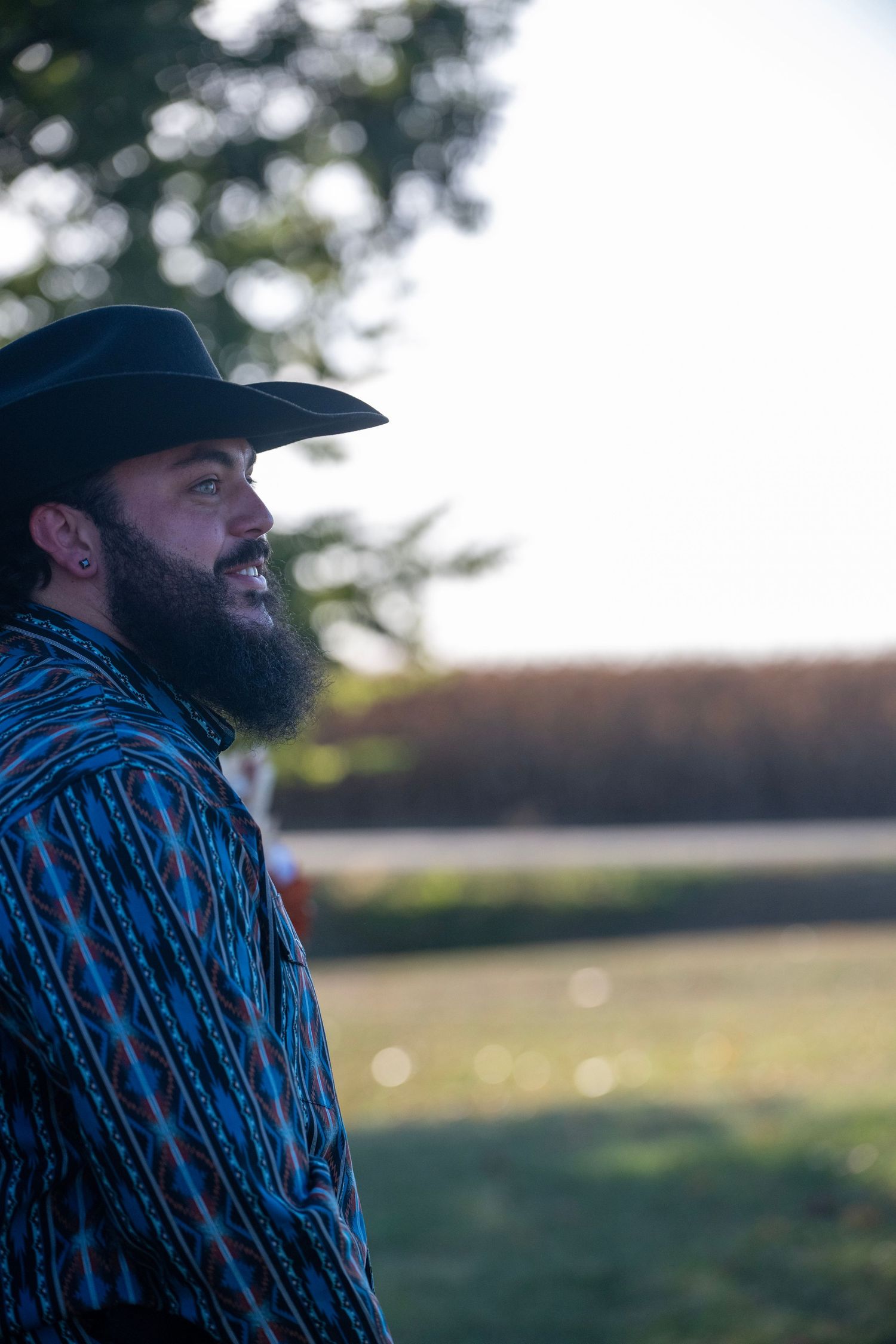 Side profile view of someone wearing a cowboy hat against a blurred outdoor background.