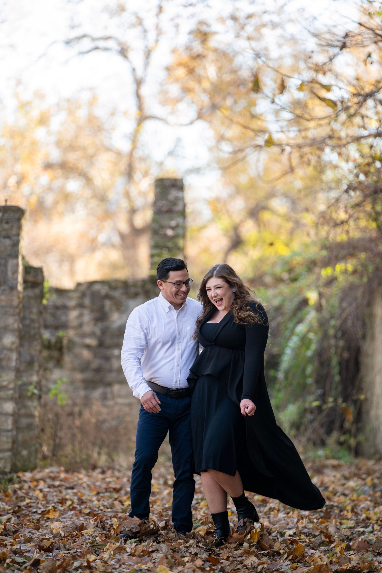 Couple shares lighthearted moment while crouching in fallen autumn leaves.