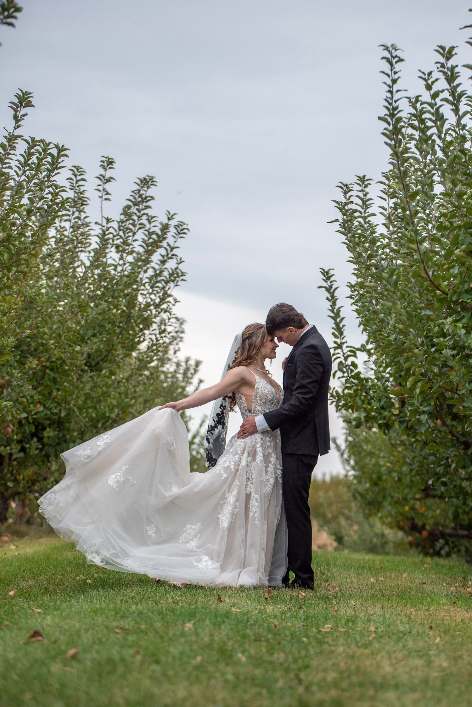 A flowing lace wedding dress catches the breeze in an orchard photoshoot.
