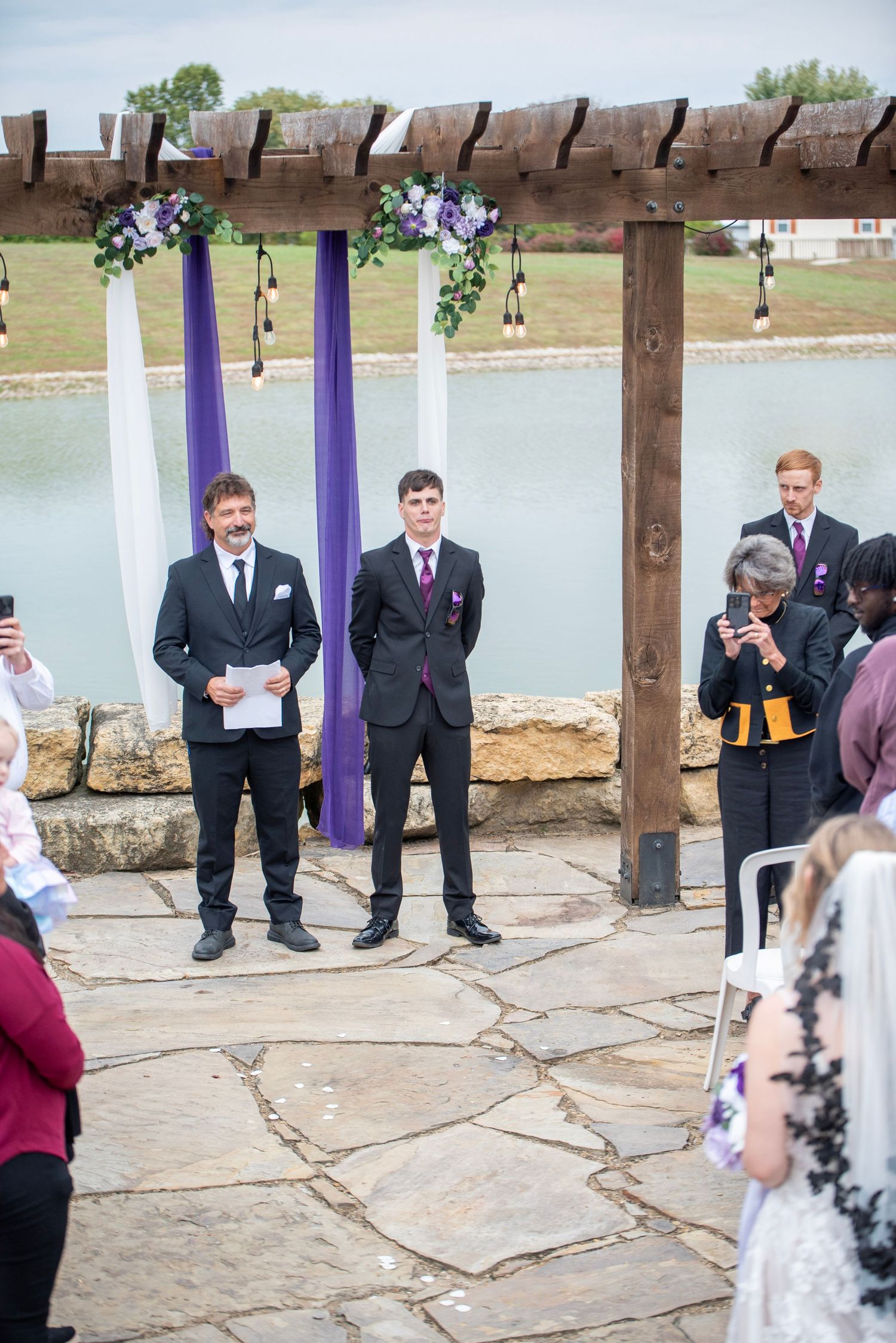 Wedding ceremony setup by a lake with purple pillars and stone flooring.