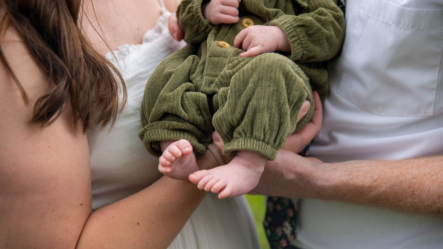 Close-up shots of hands holding and interacting with a baby in green clothing.