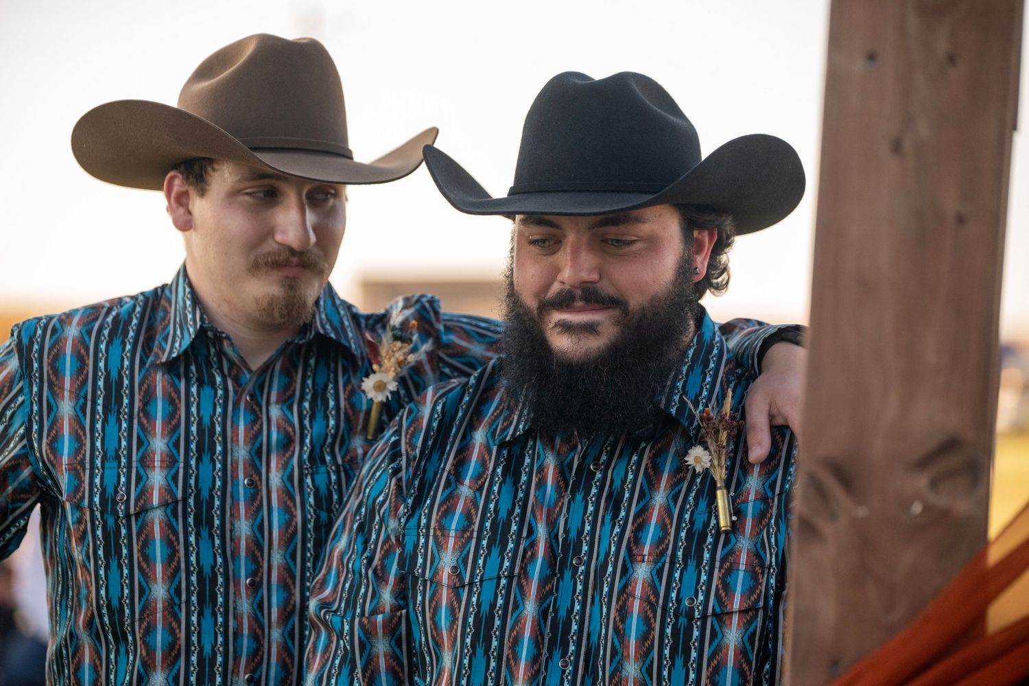 People in western shirts and cowboy hats gather under a wooden structure.