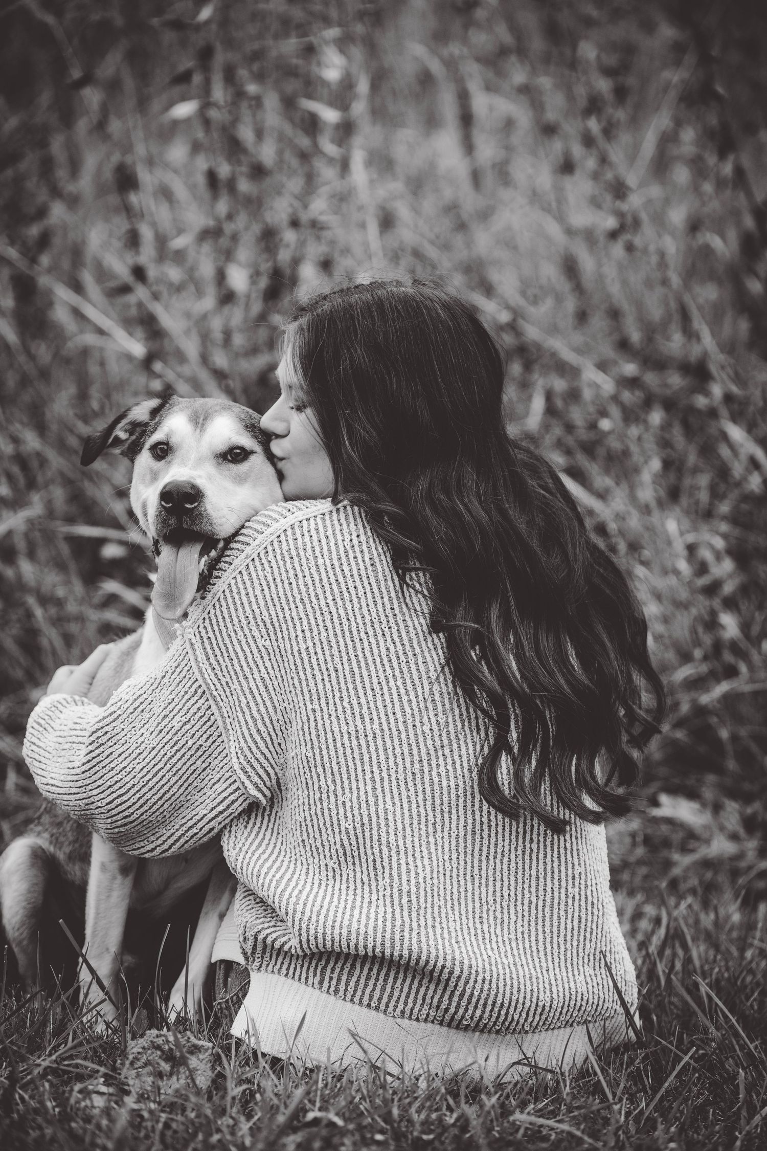 A black and white portrait captures tender moment between a dog and person in a sweater.