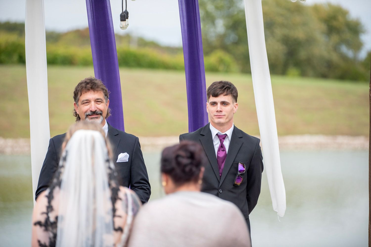 Outdoor lakeside wedding ceremony with white and purple decorative elements.