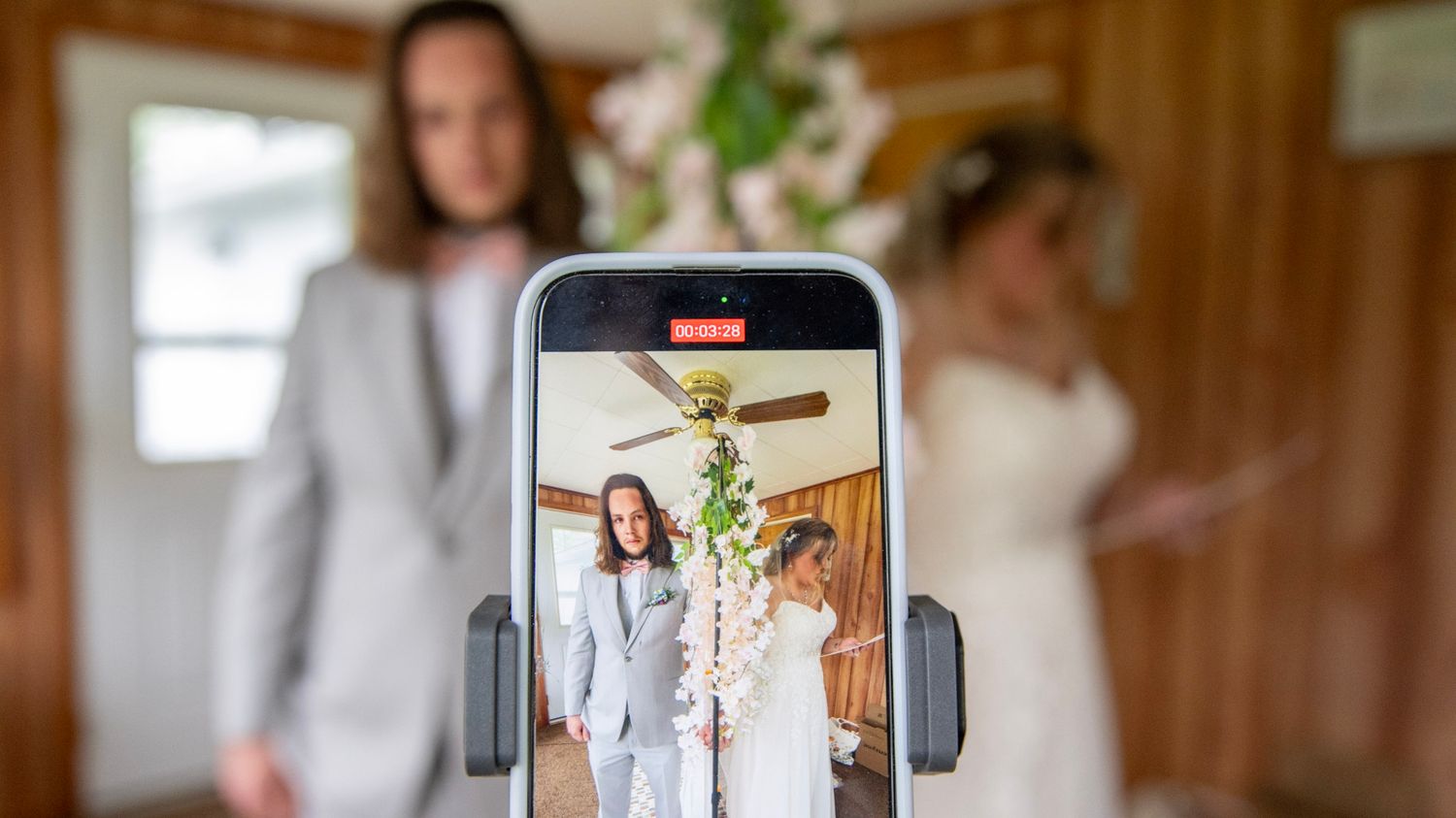 Phone capturing wedding photo through hanging floral arch.