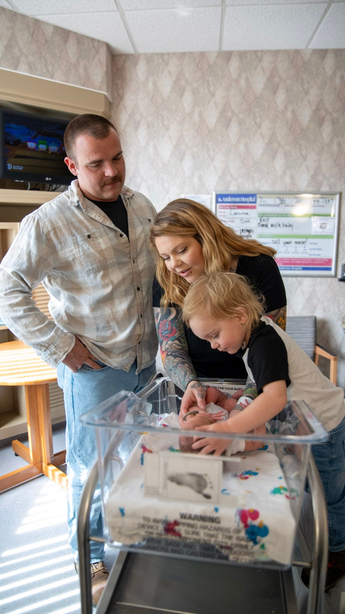 Family gathering around a hospital bassinet to look at a newborn.