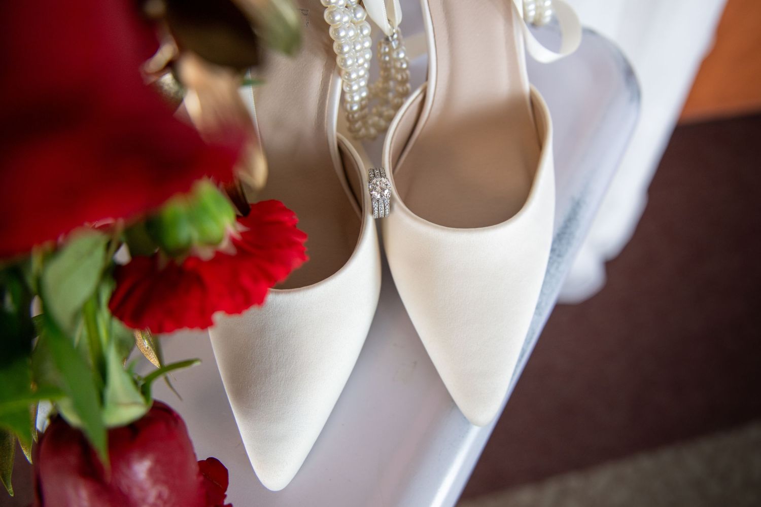 Wedding detail shot of white bridal shoes with red floral accents.