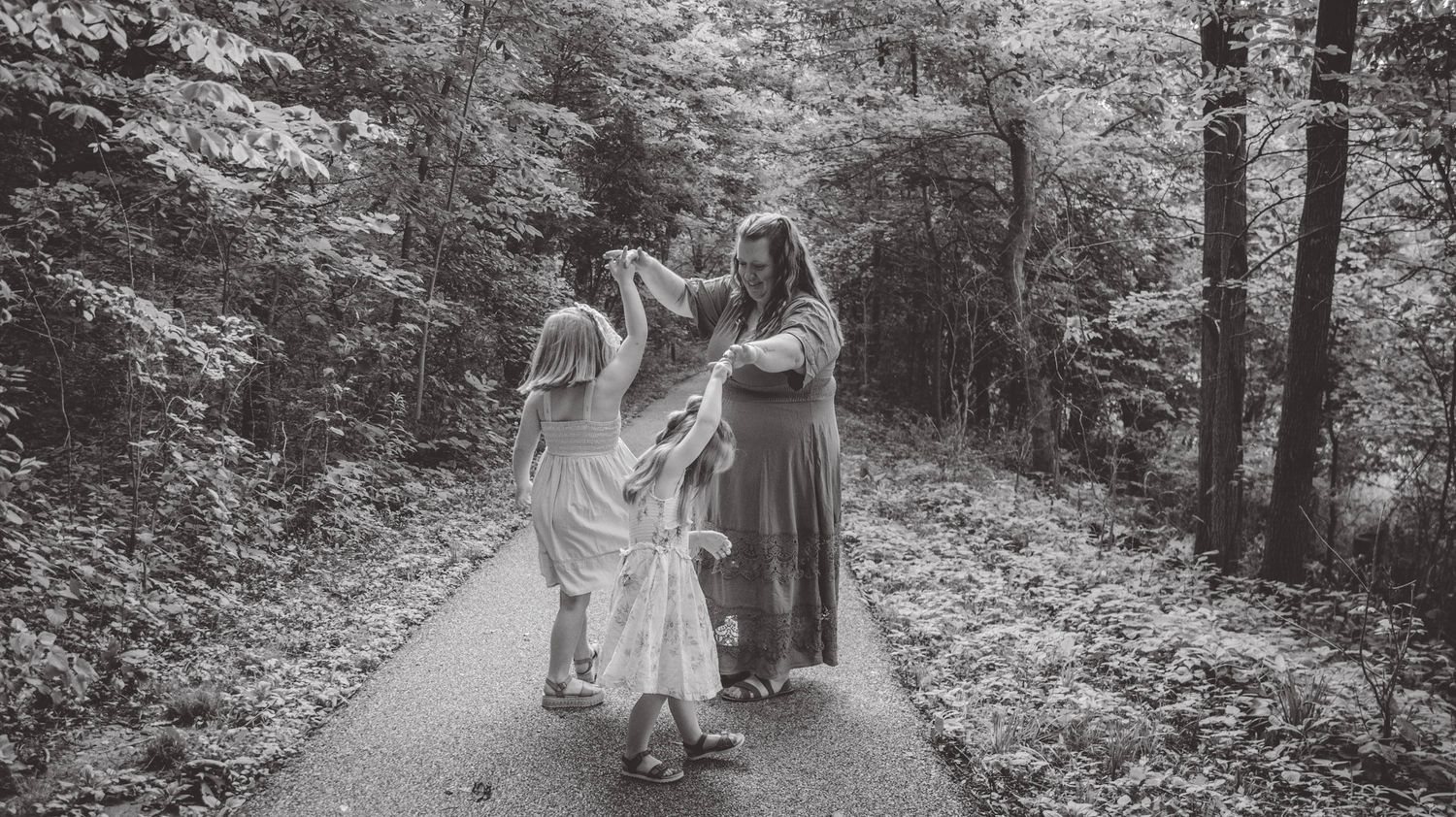 Three people walk together on a forest path in black and white.