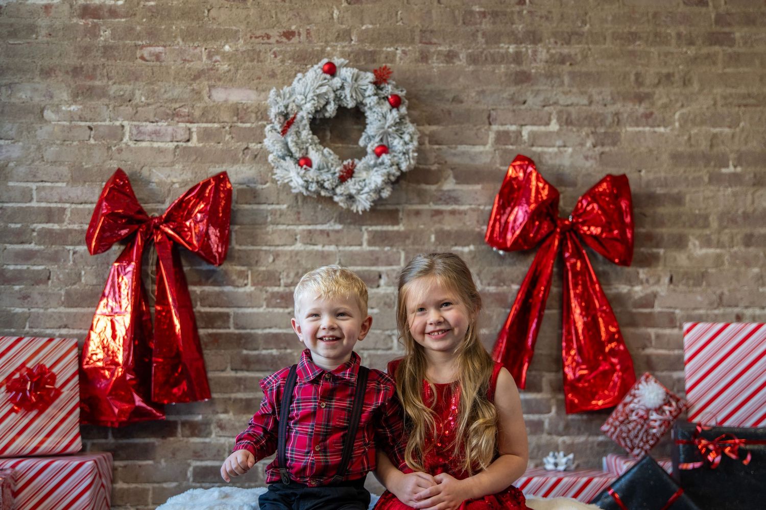 Holiday portraits with red bows and festive decorations against rustic brick wall.
