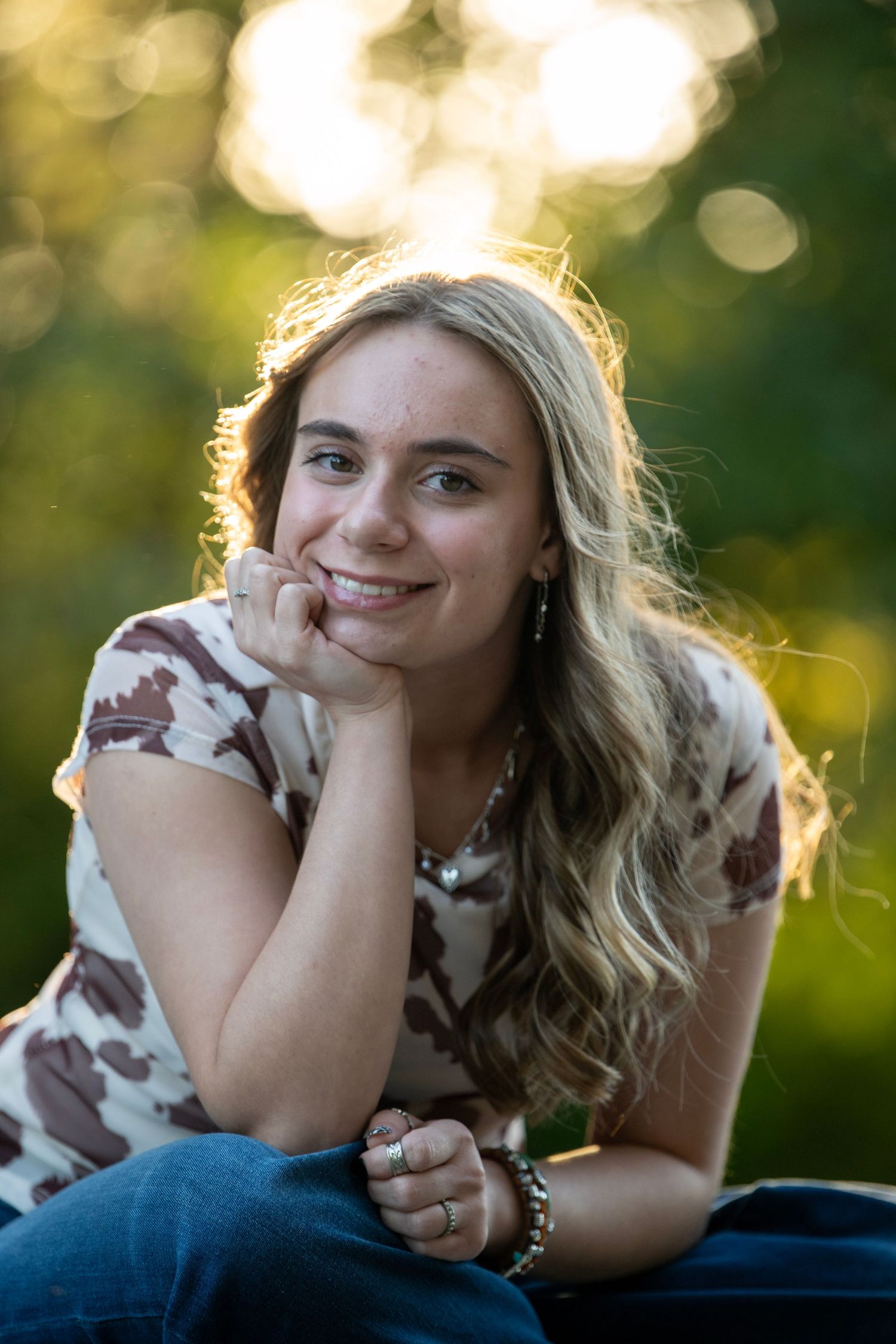 Casual outdoor portrait with someone in a cow print top and blue jeans relaxing on the ground.
