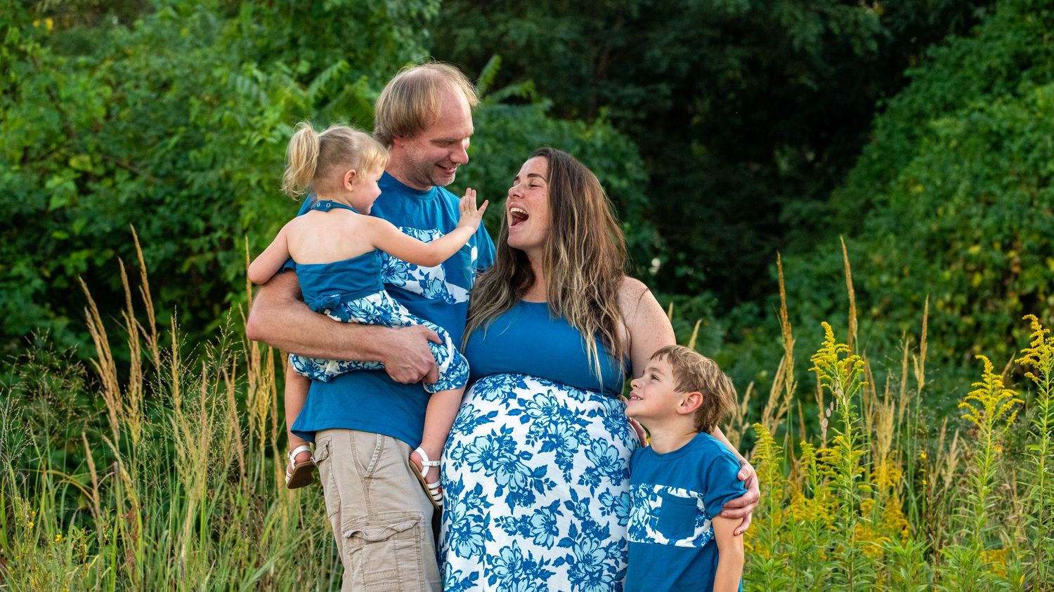 Wide angle nature shot of a family photo session among tall grass and trees.