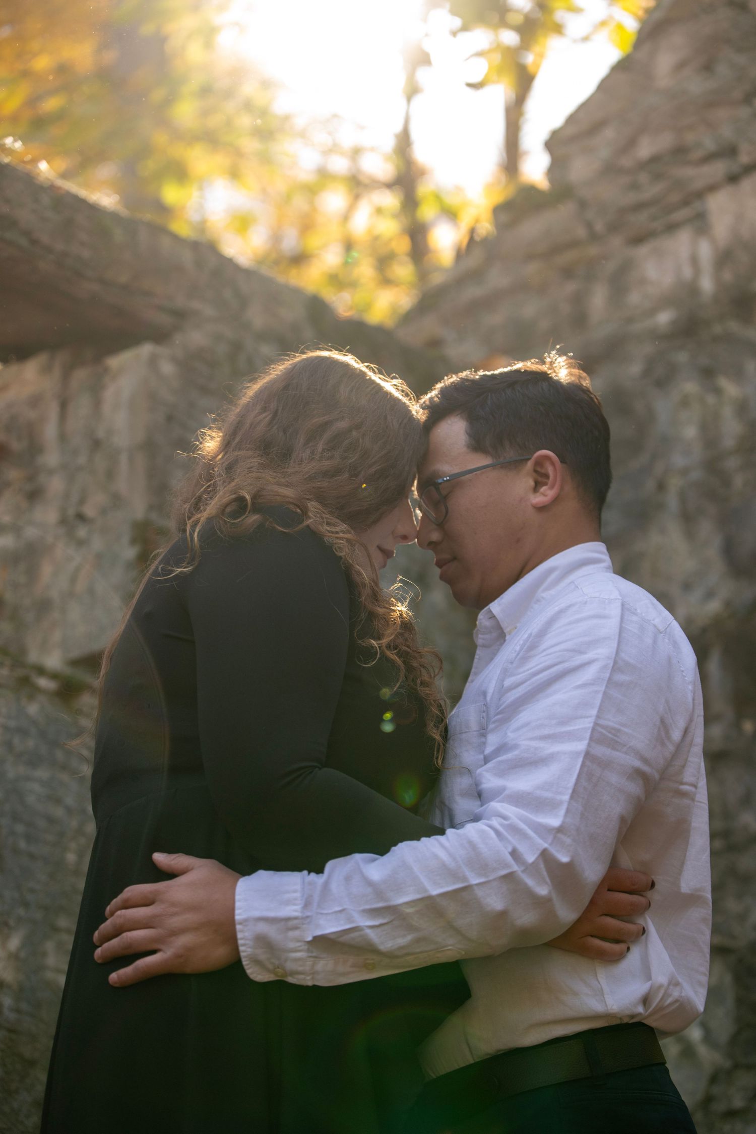 A romantic embrace captured in golden sunlight between historic stone columns.