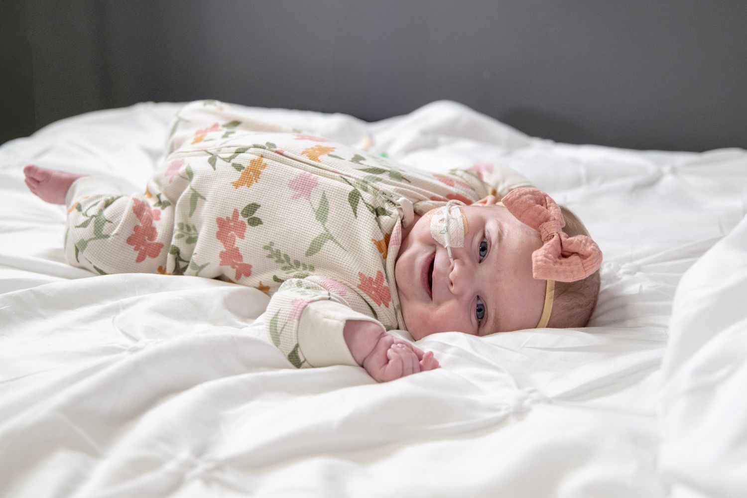 A newborn baby rests peacefully on white floral bedding in a lifestyle photography session.