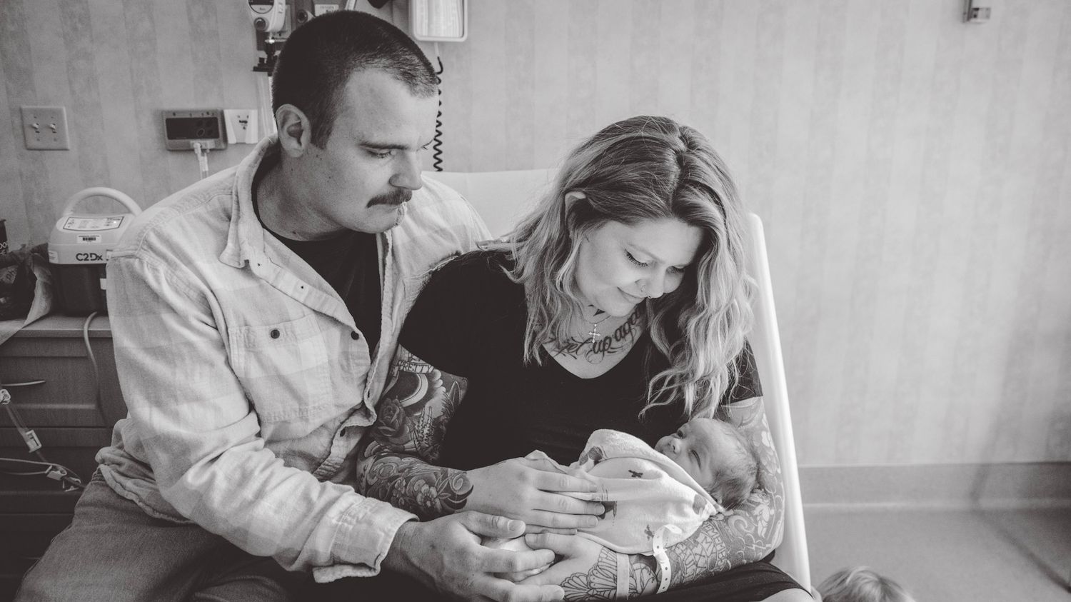 Monochrome wide shot of a hospital room where parents are bonding with their newborn.