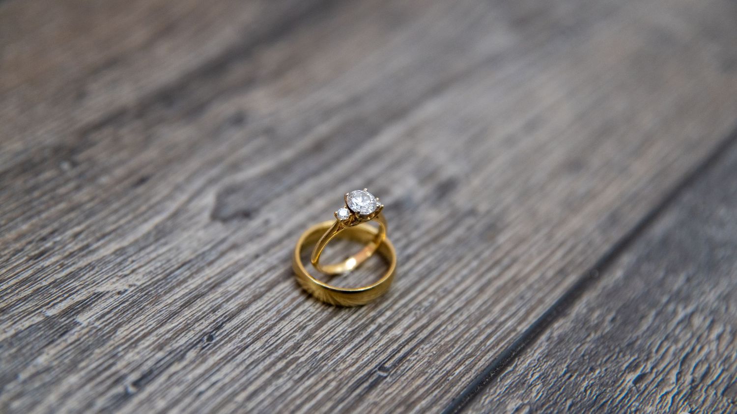 Gold wedding rings photographed on a rustic gray wooden surface.