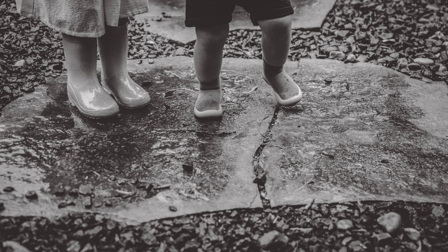 Close-up view of feet and legs standing on wet pavement with scattered leaves.