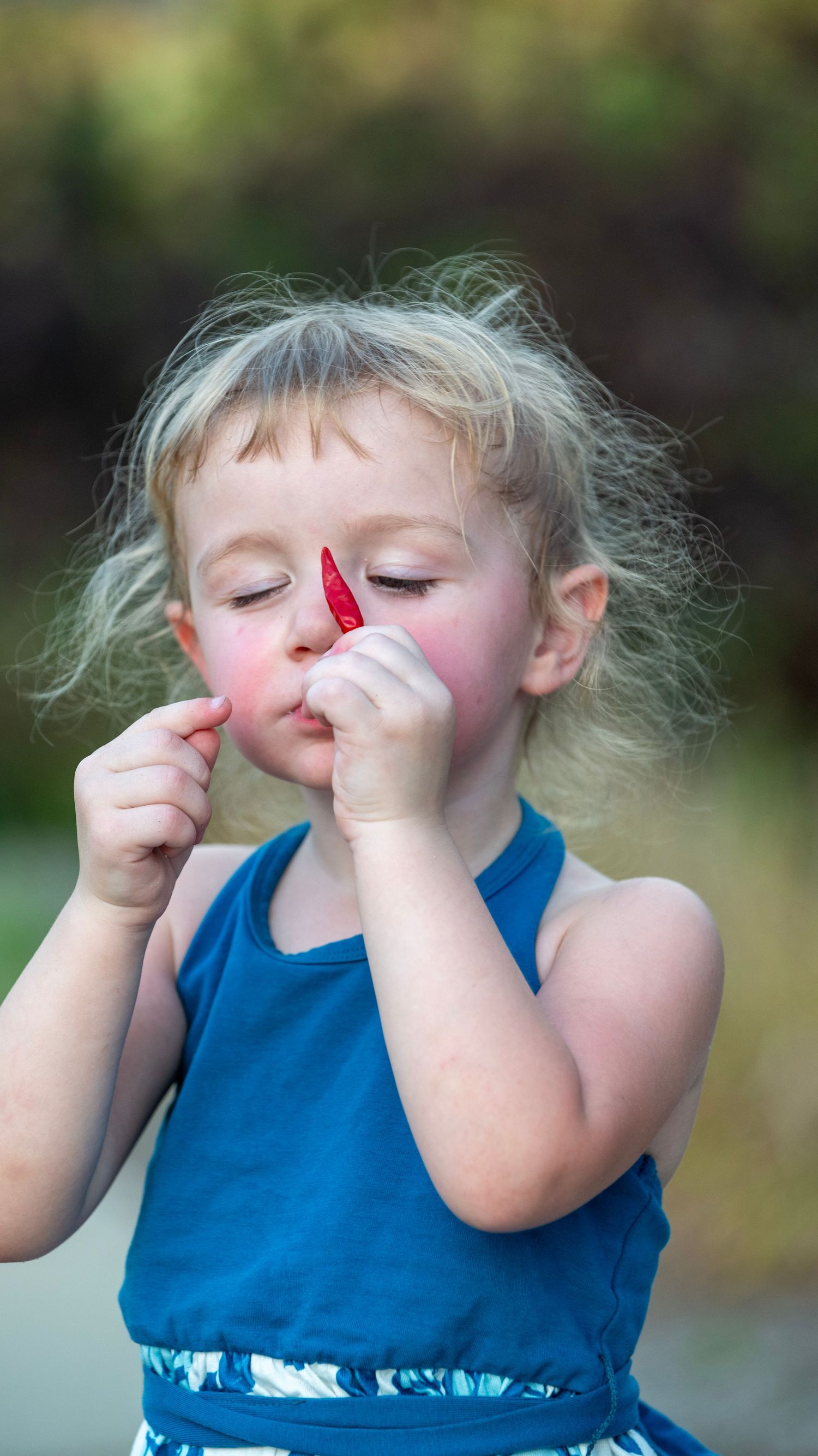 Child in blue dress making silly faces and gestures in outdoor portrait sequence.