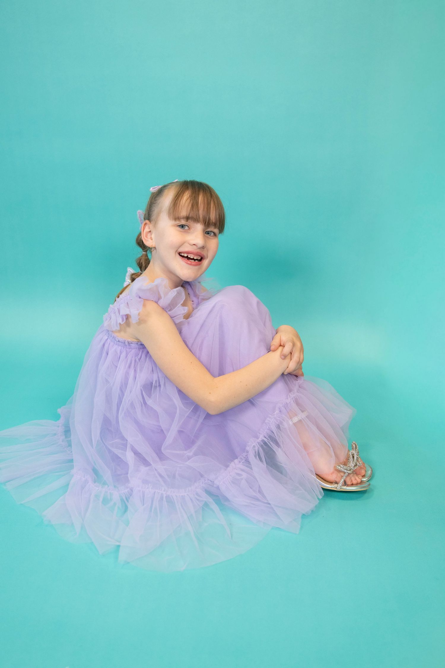Whimsical pose in a lilac tulle dress with butterflies on turquoise background.