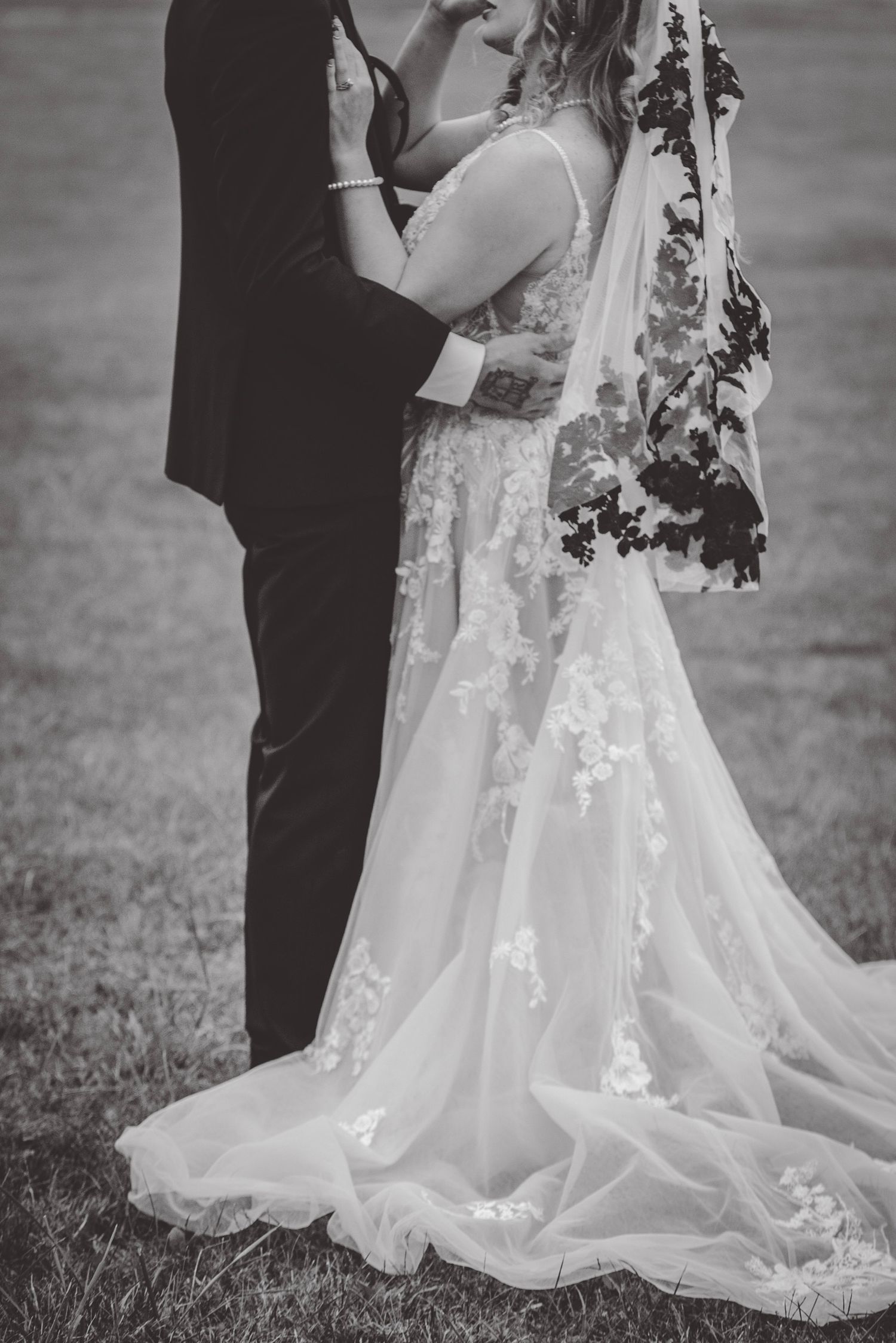 Intimate black and white portrait of couple embracing, showcasing detailed lace wedding gown.