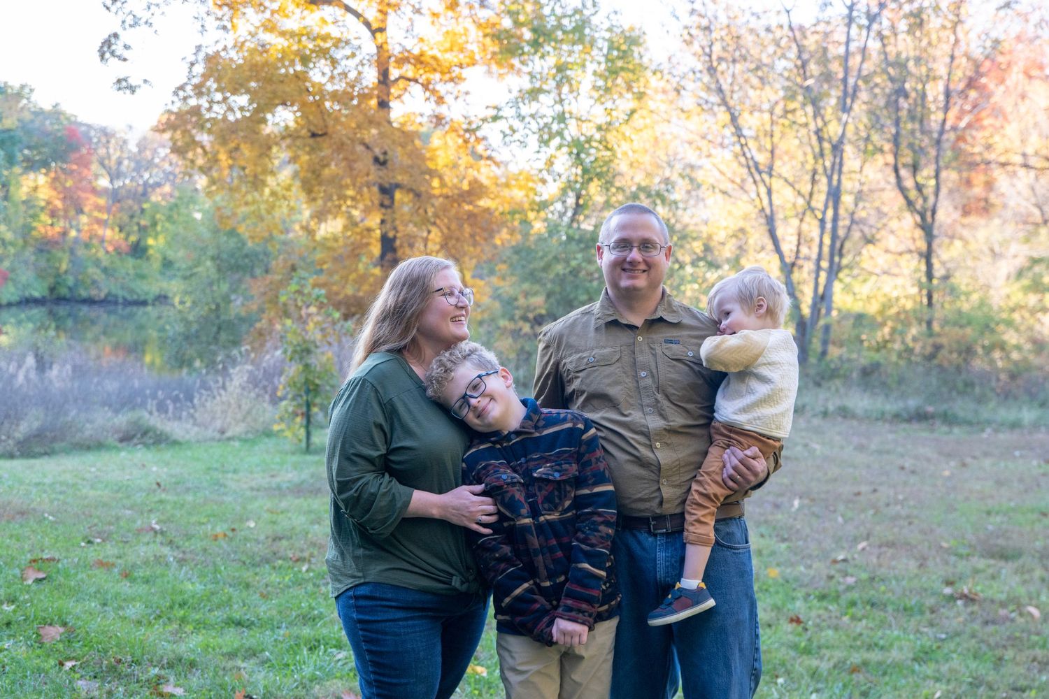Family gathering outdoors in a meadow with autumn trees creating a scenic backdrop.