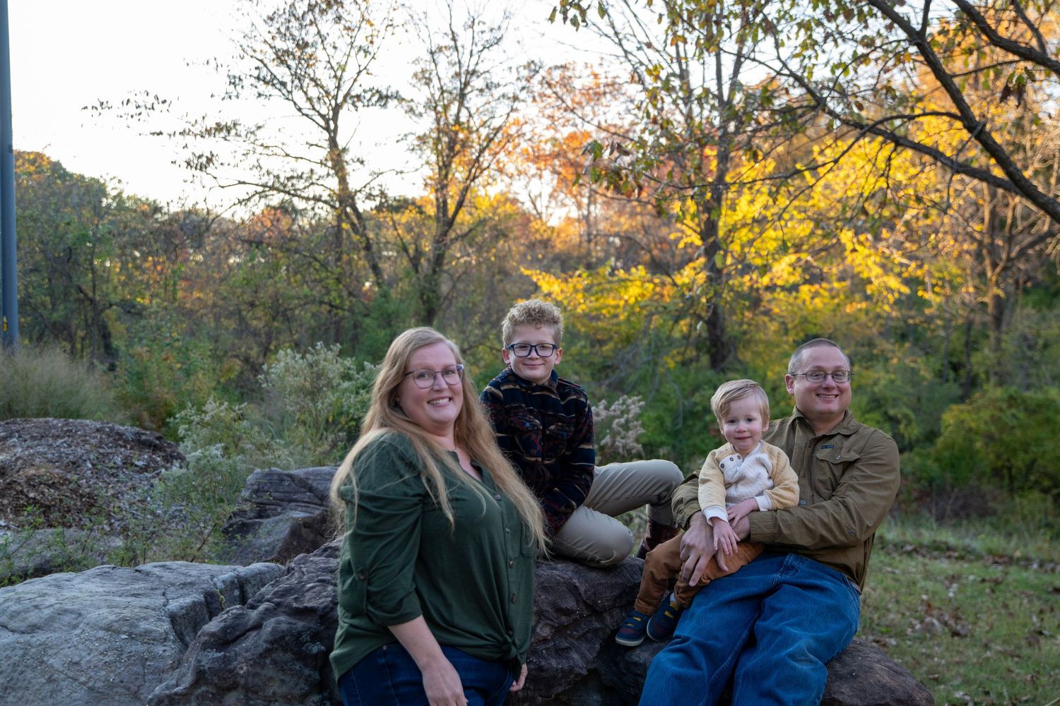 A family sits together on rocky terrain surrounded by autumn foliage at sunset.